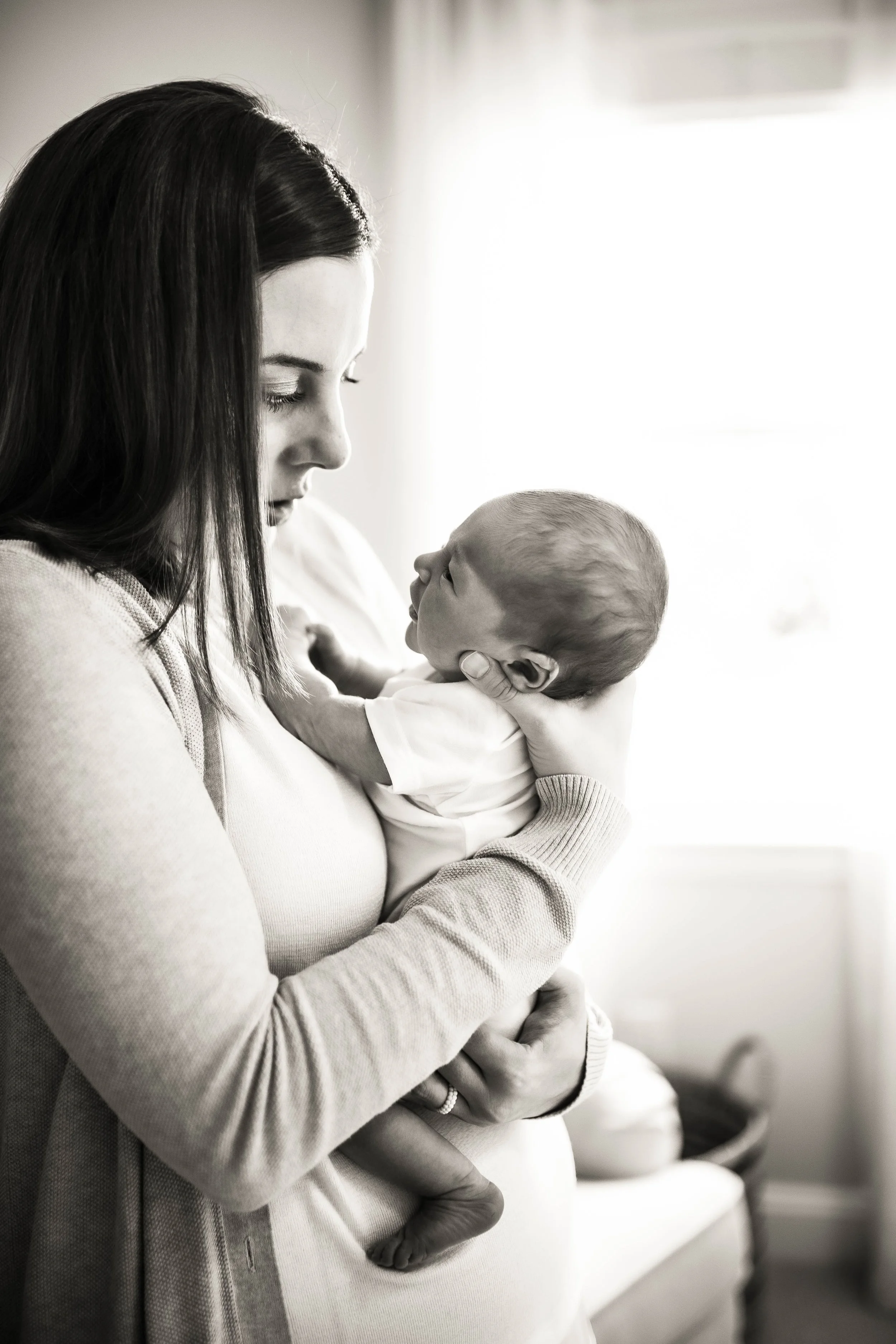 A woman holding a baby close to her chest, with their foreheads nearly touching, in a softly lit room.