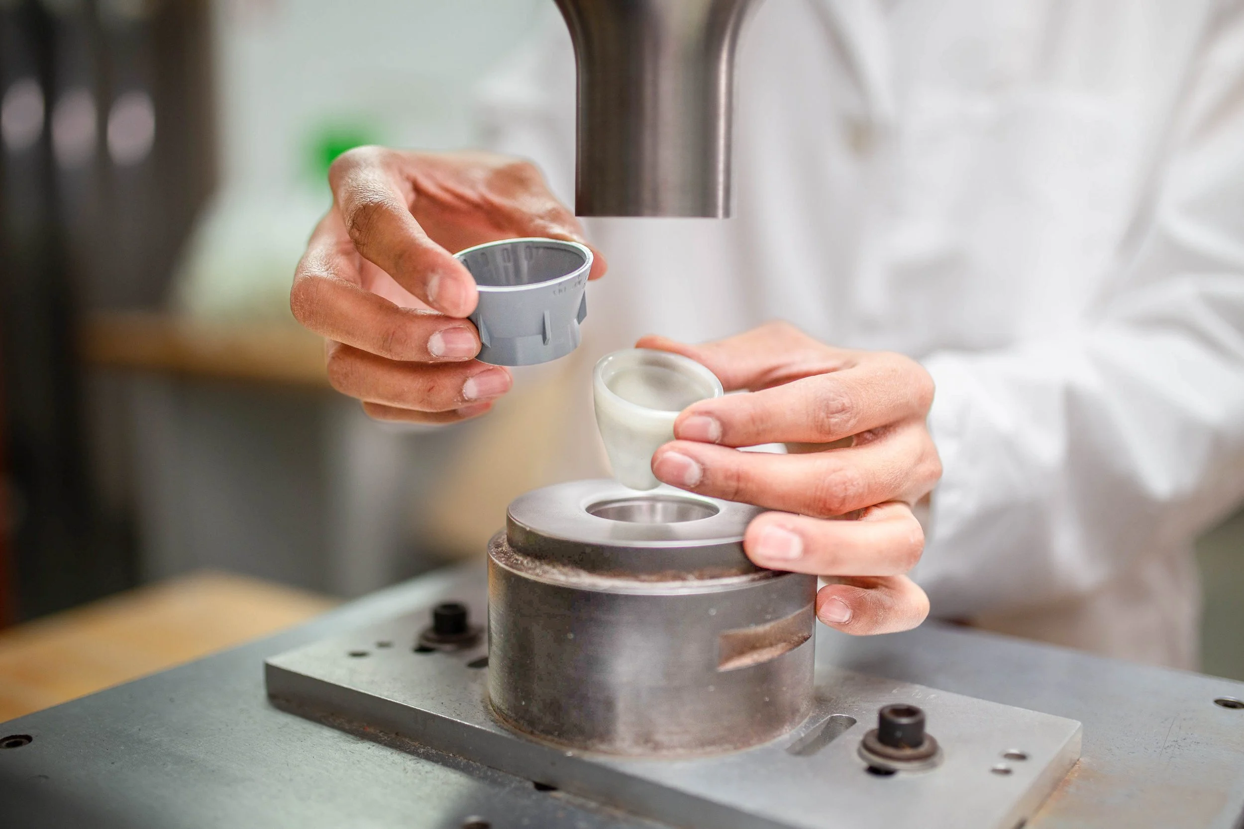 A person in a white lab coat is working with a small ceramic component, placing it into a metal mold on a machine, possibly for testing or manufacturing purposes.