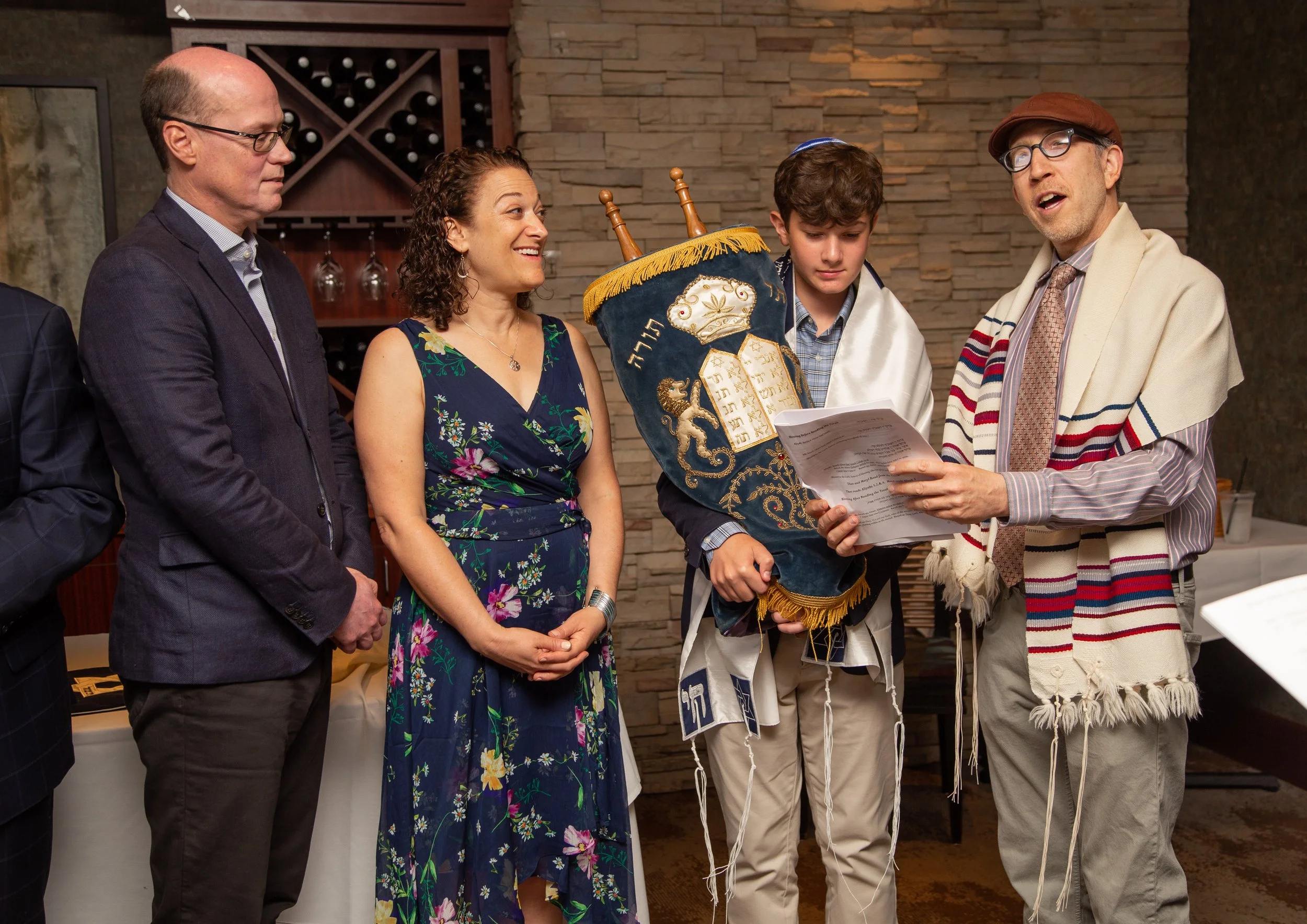Group of Jewish individuals participating in a Bar Mitzvah ceremony, with one person reading from a script and others observing.