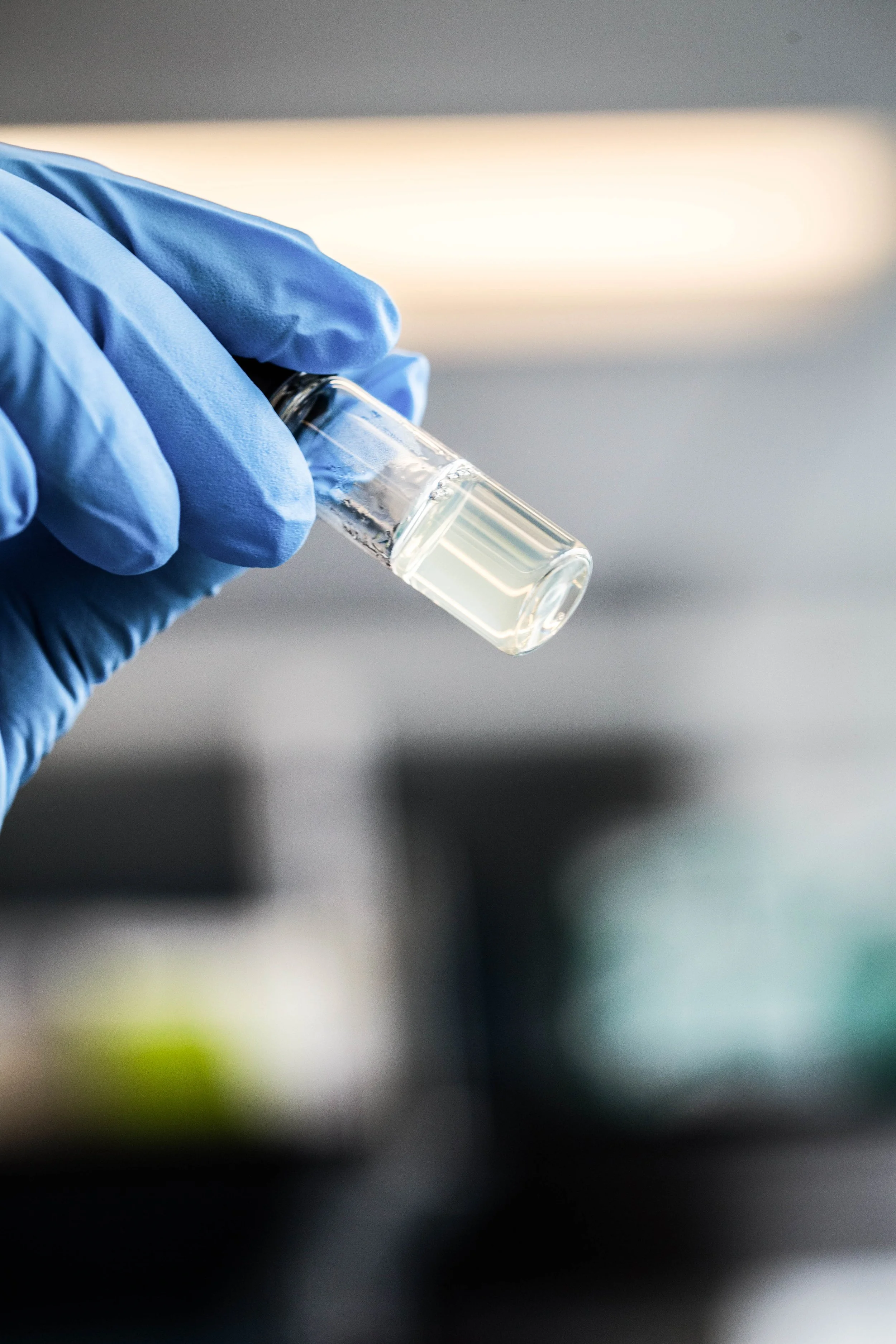 A gloved hand holding a small test tube with a clear liquid.