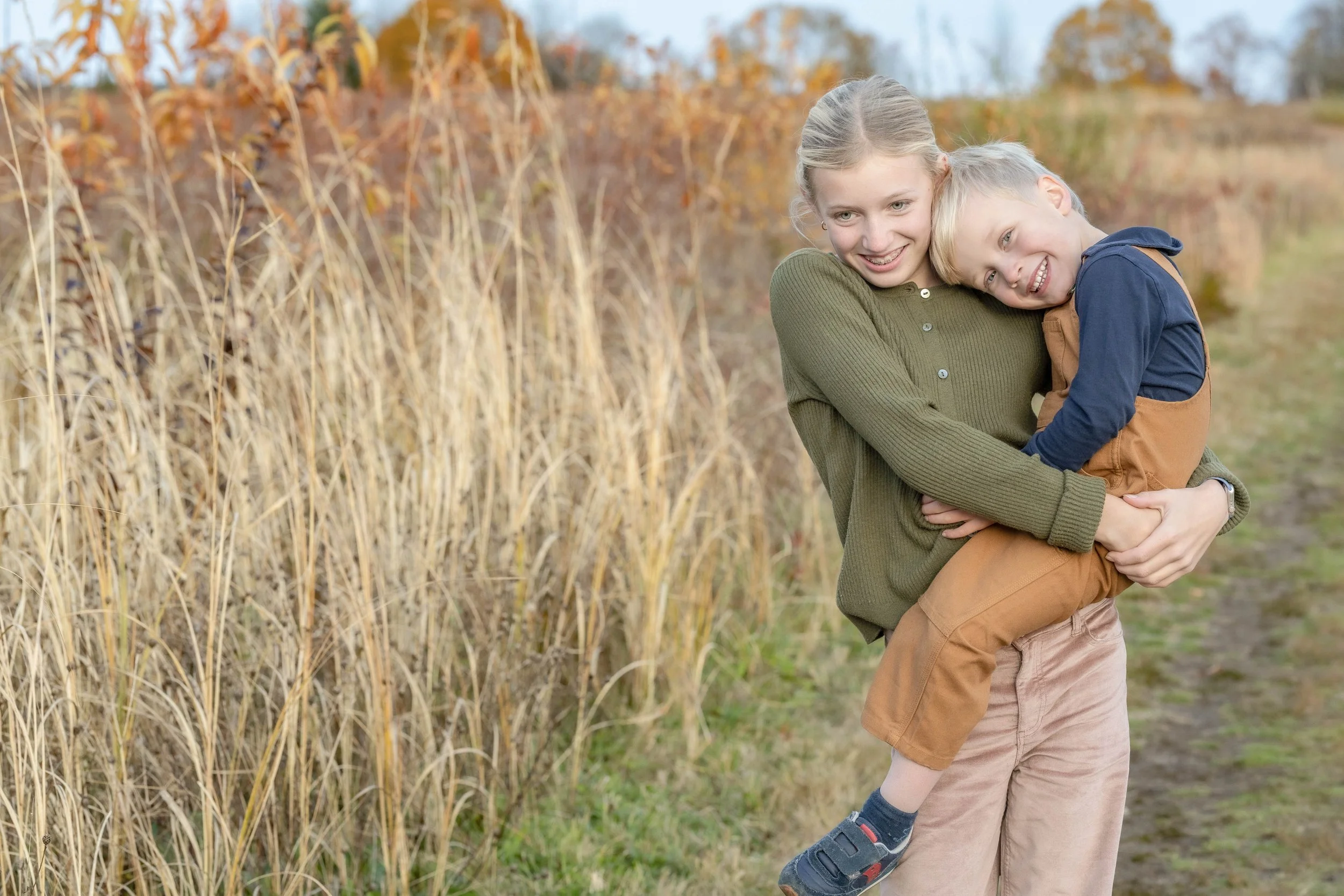 A woman holding a young boy in her arms on a fall day near a field of dry corn stalks.