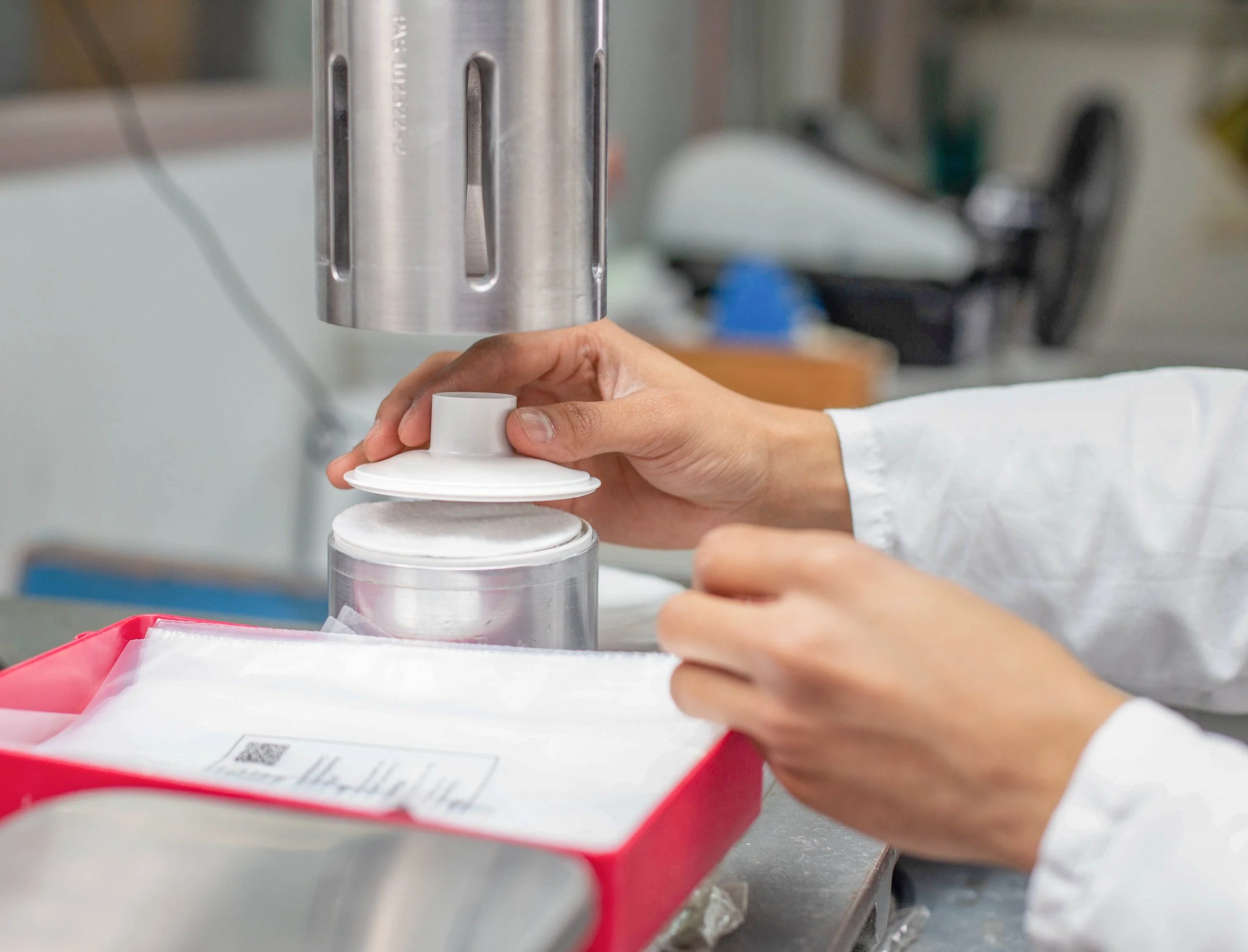A person using a machine to prepare medical supplies with white gloves and a white lab coat, with medical packaging nearby.