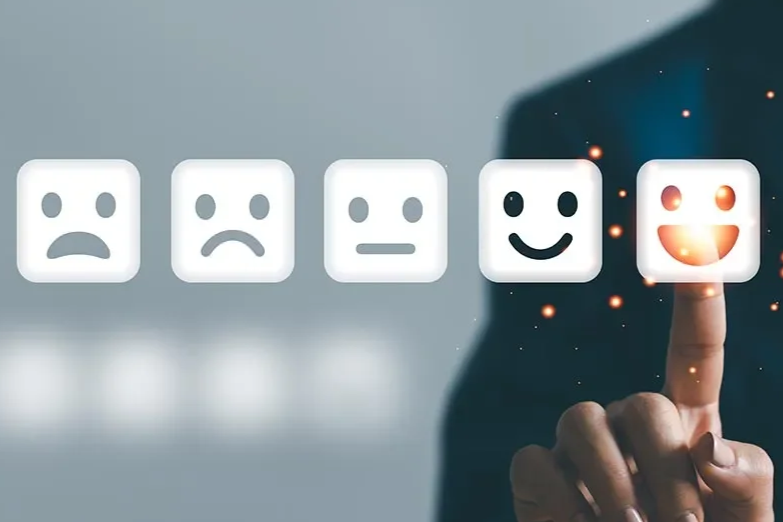 A person touching a digital interface with five emoji faces displaying different emotions: sad, unhappy, neutral, happy, and very happy.