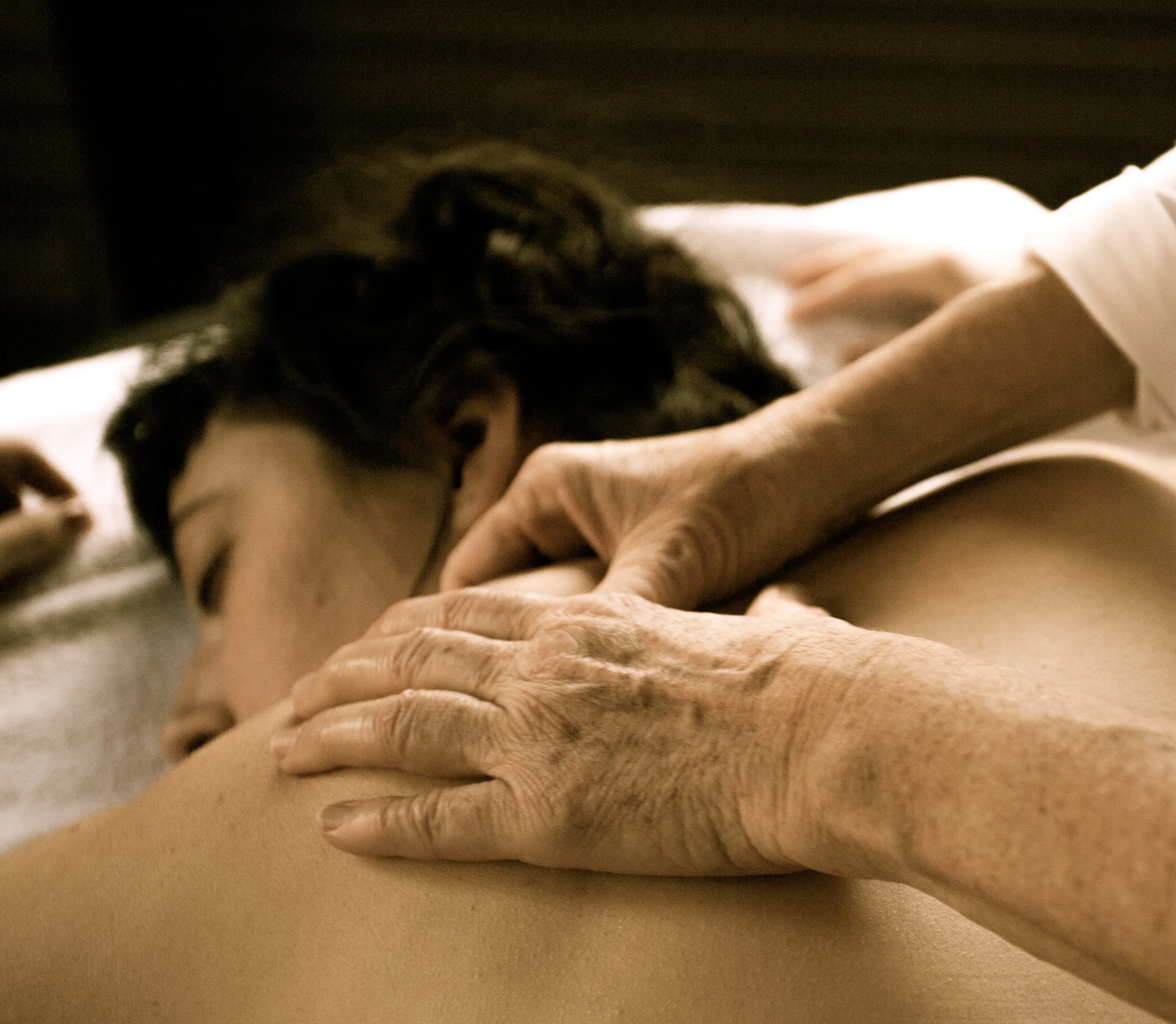 Eine Person schläft friedlich auf einer Couch oder einem Bett, während eine ältere Hand diese hält, was Zuneigung und Fürsorge zeigt.