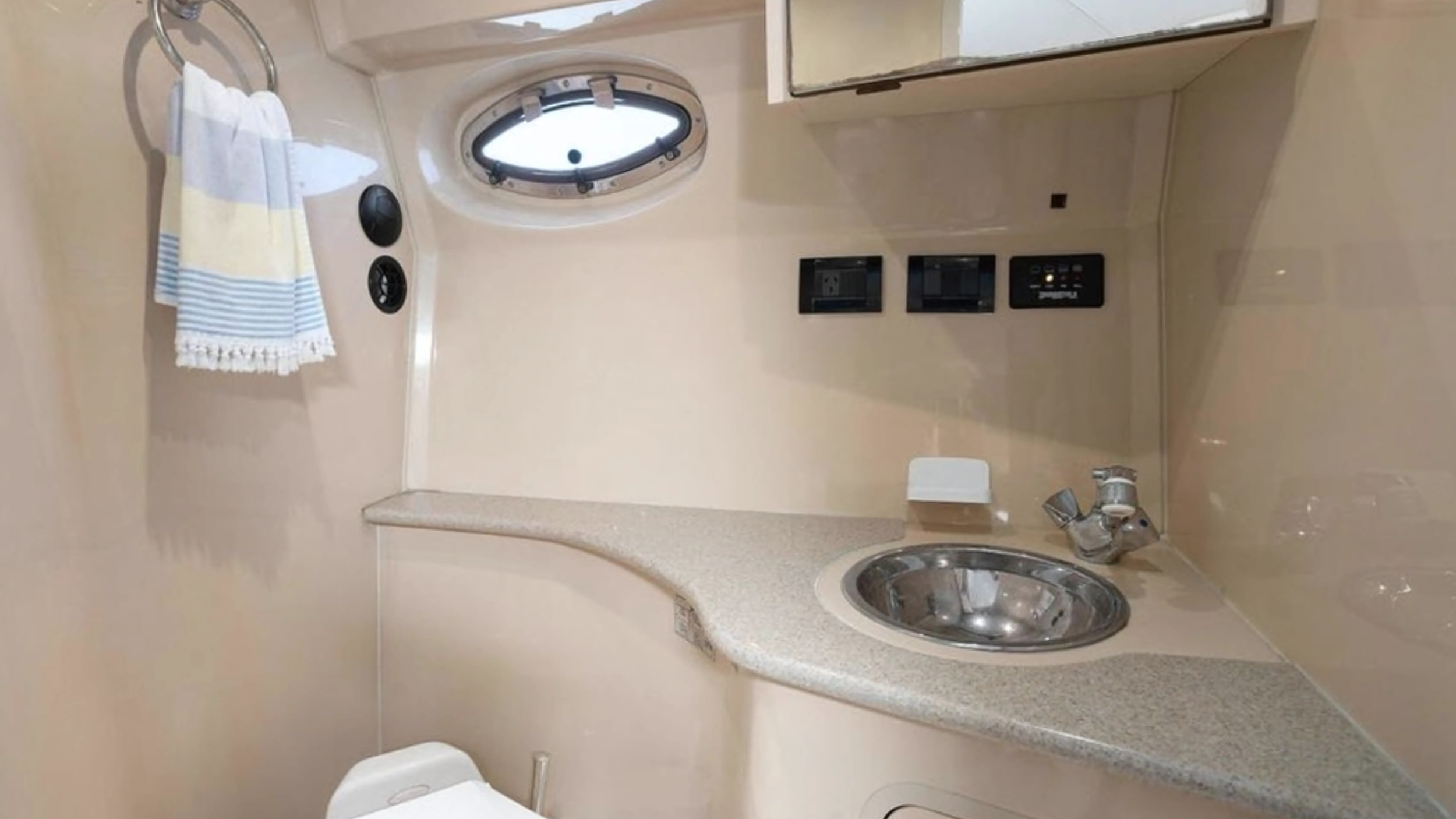 Compact bathroom with a small round window, a stainless steel sink, and beige walls.