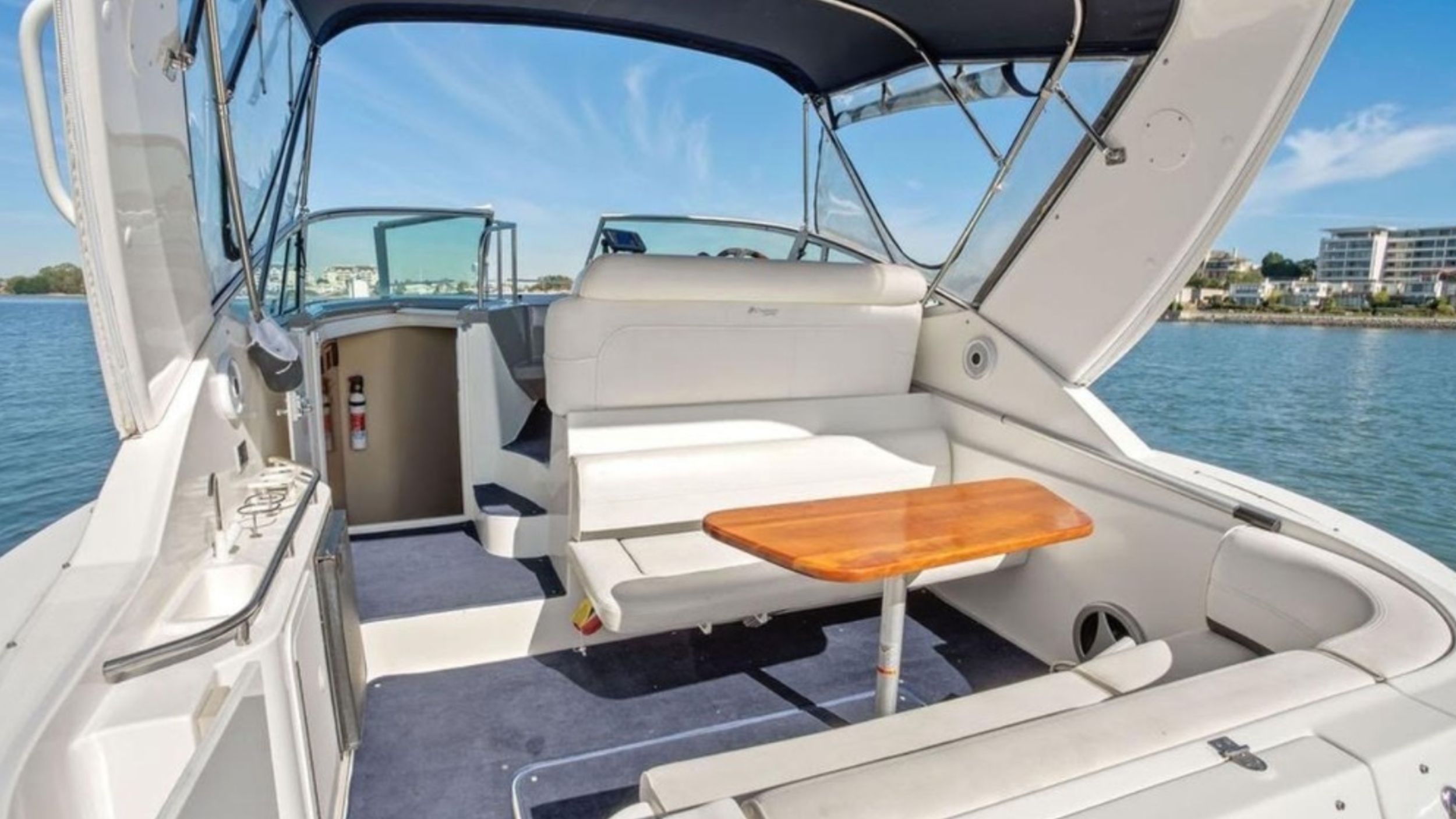 Interior of a motorboat with white seating, wooden table, and water view