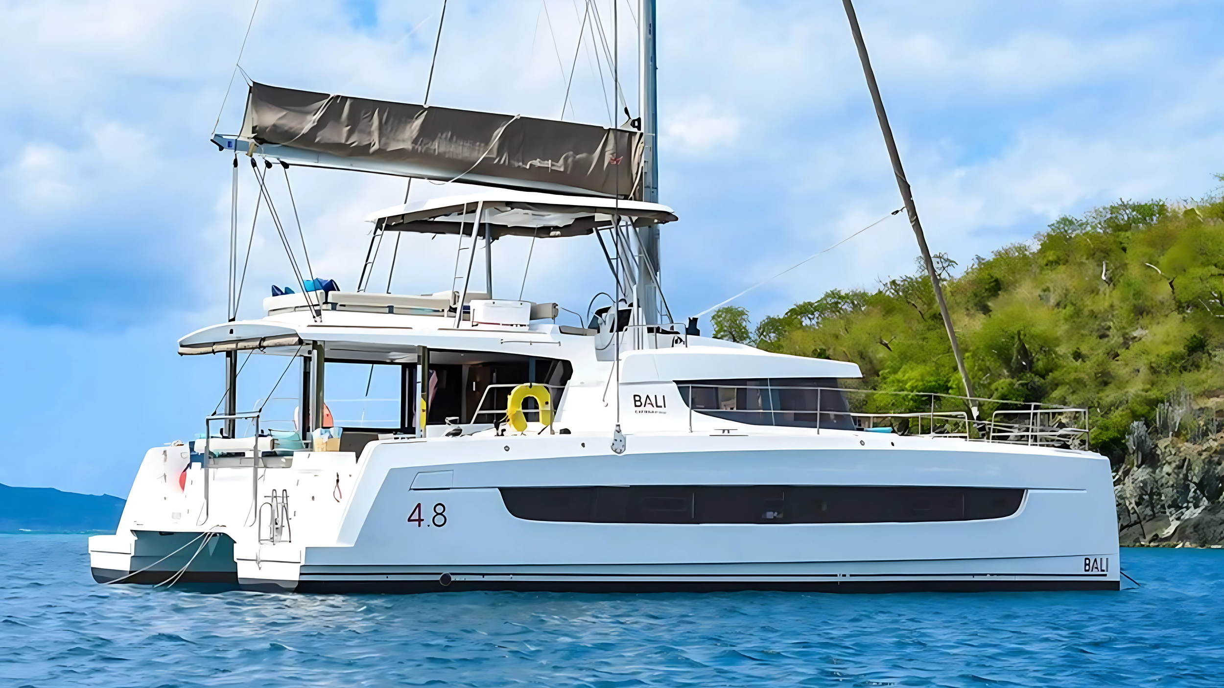 Luxury catamaran yacht sailing on clear blue water with green islands in the background.