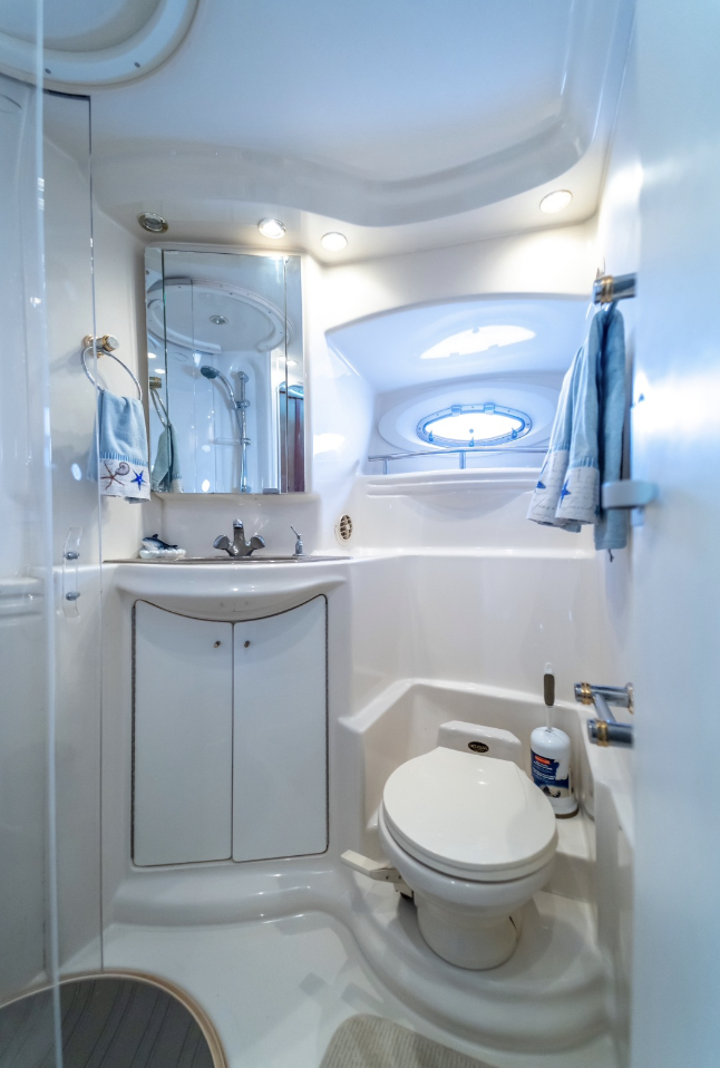 Compact yacht bathroom with toilet, sink, mirror, towels, and round window.
