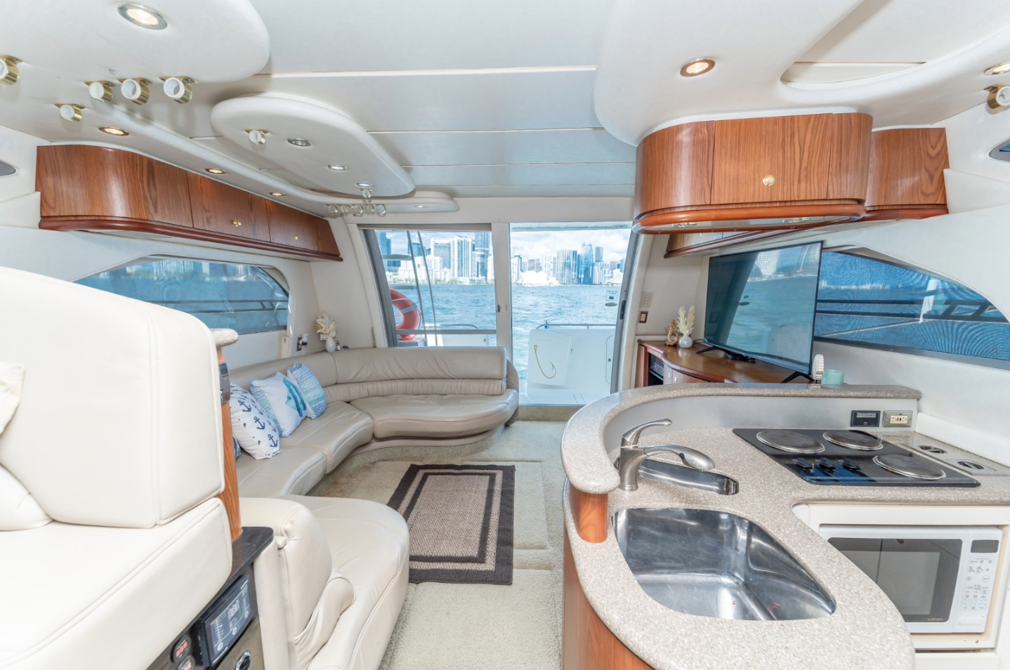 Luxury yacht interior with sofa, kitchen area, and city view from windows.