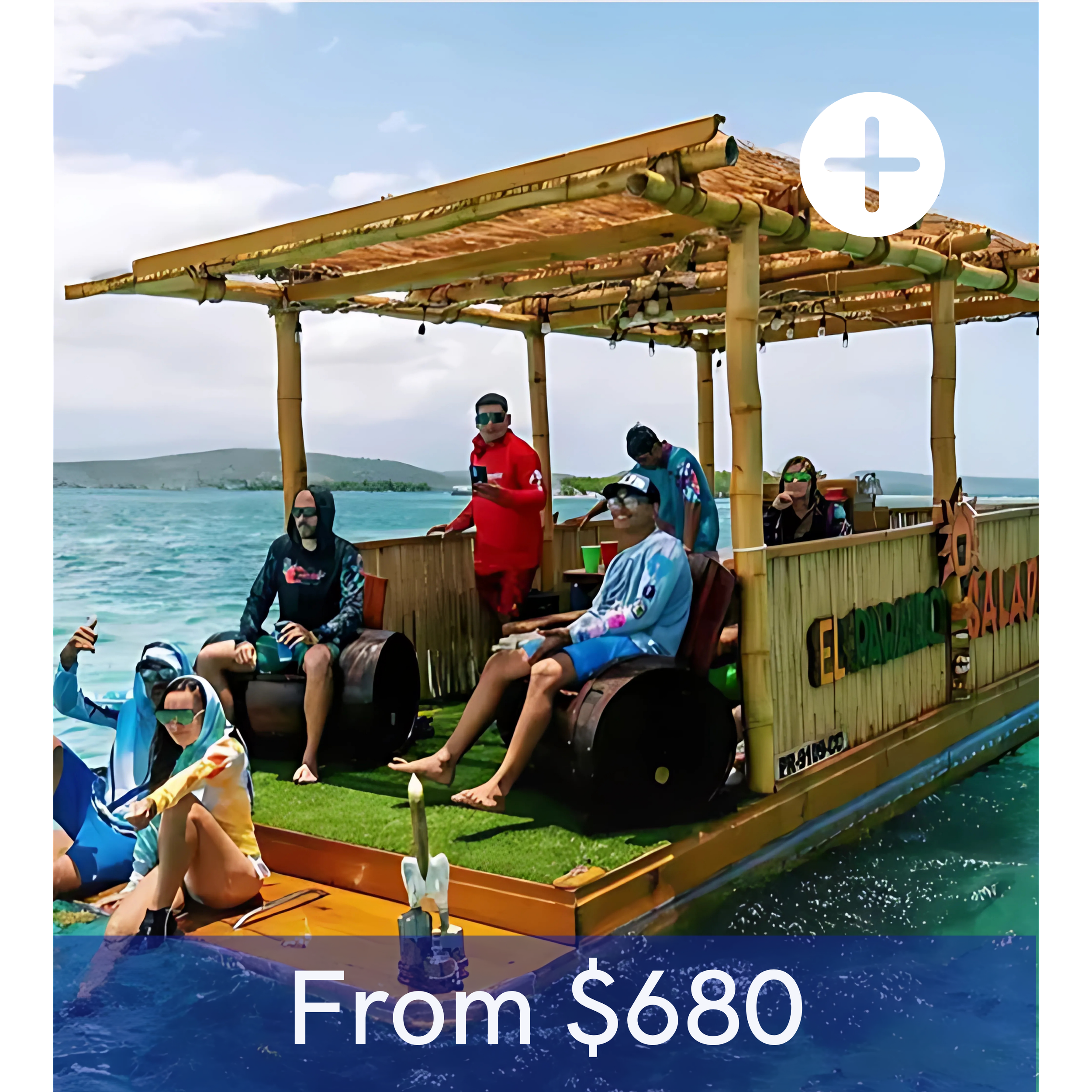 A group of people on a float boat shaped like a wooden raft with a bamboo roof, floating on the water. The boat has colorful decorations and sign that reads 'El Flotador'. People are sitting and standing, some are taking photos, all enjoying sunny weather and water scenery.