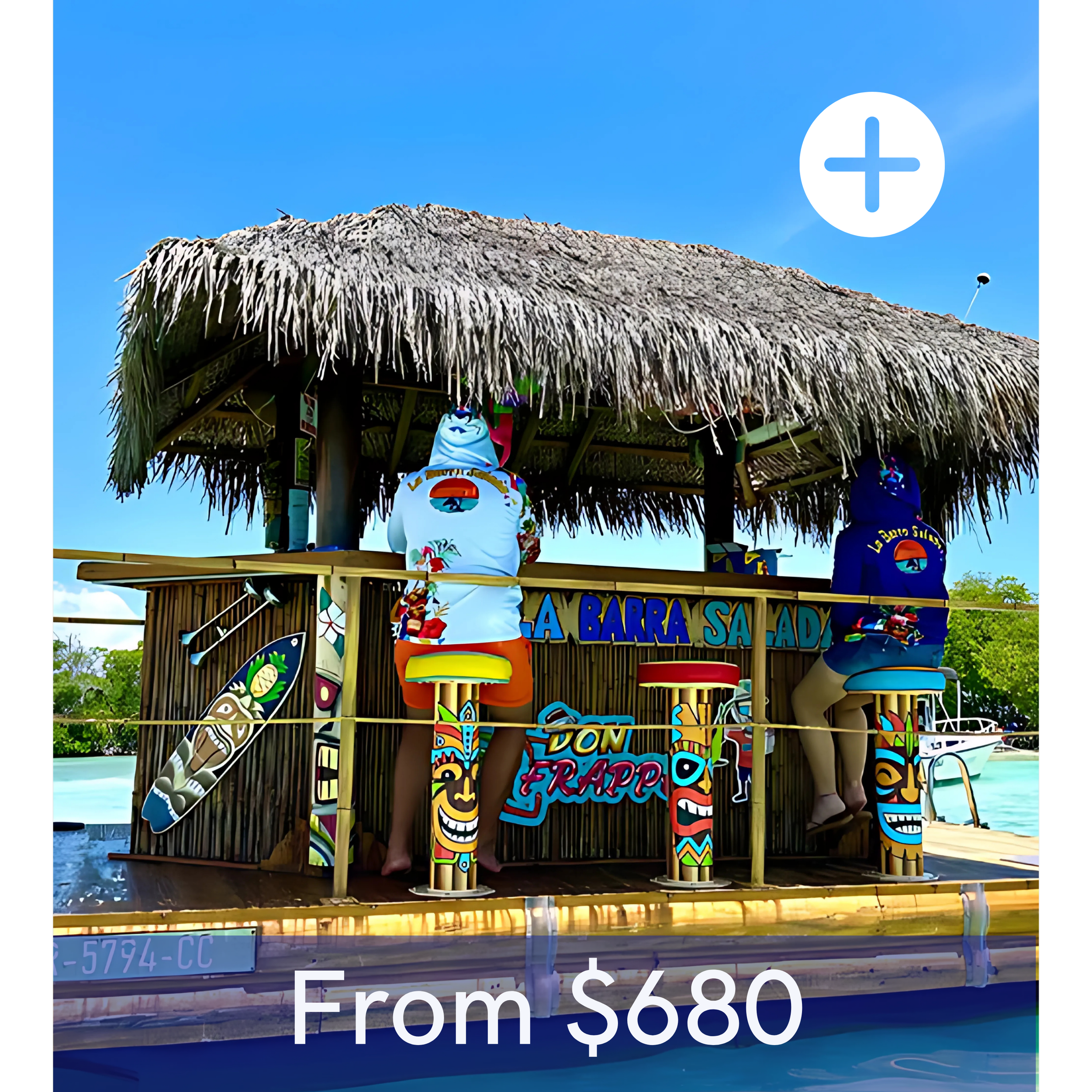 A tiki bar on a boat with a thatched roof, decorated with colorful tiki statues, signs, and surfboard decorations, set against a clear blue sky with water and greenery in the background.