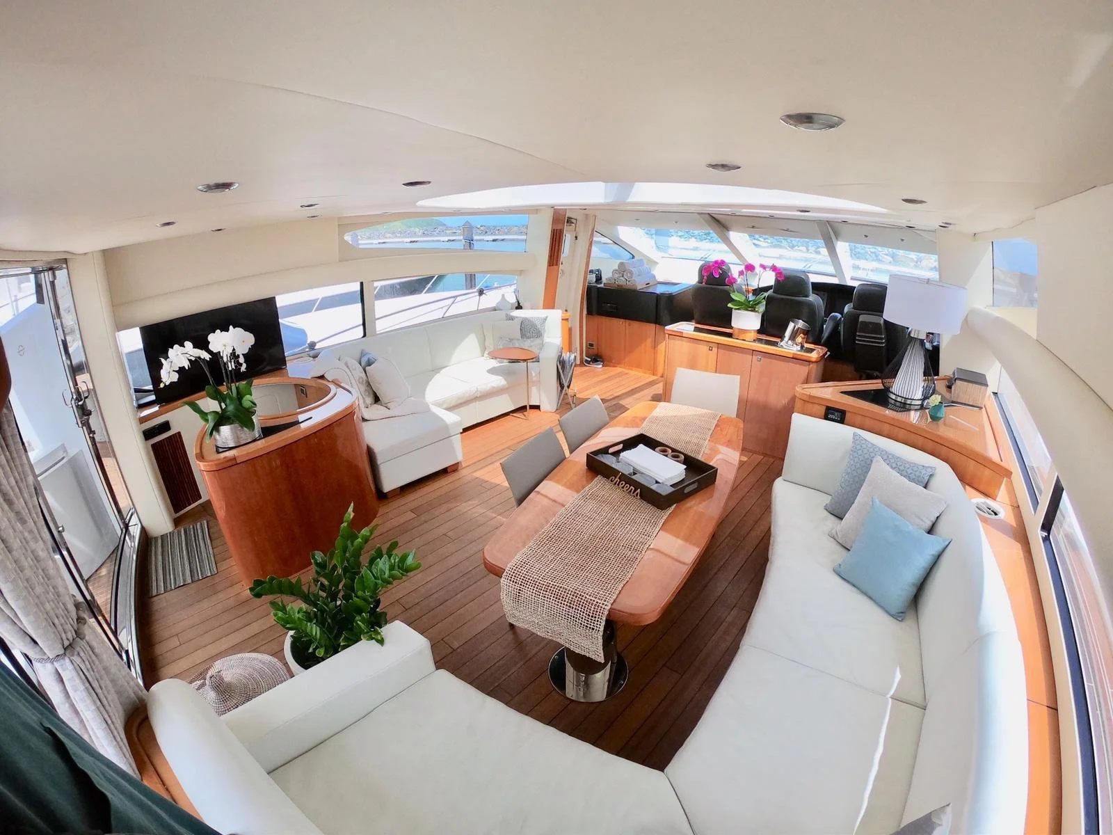 Luxurious yacht interior with white sofas, wooden flooring, decorative plants, and large windows.