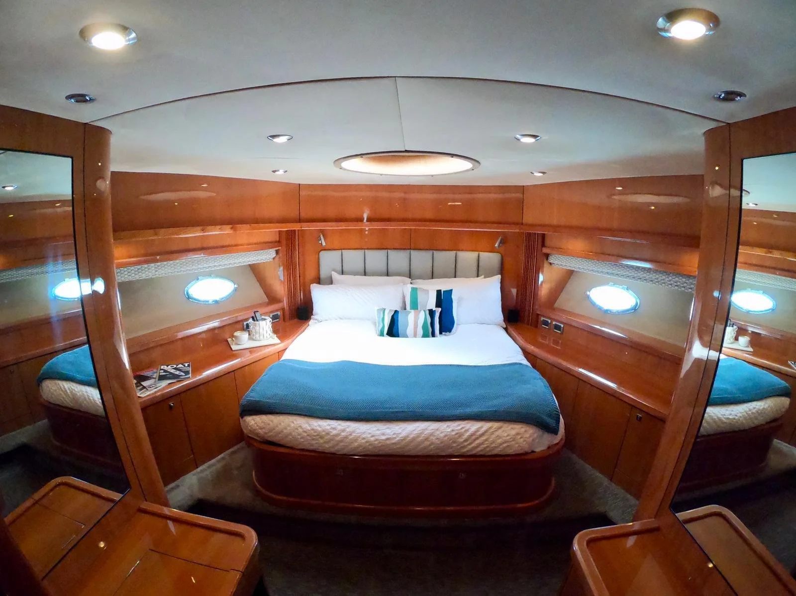 Luxury yacht cabin interior with bed, wood paneling, portholes, and overhead lights.