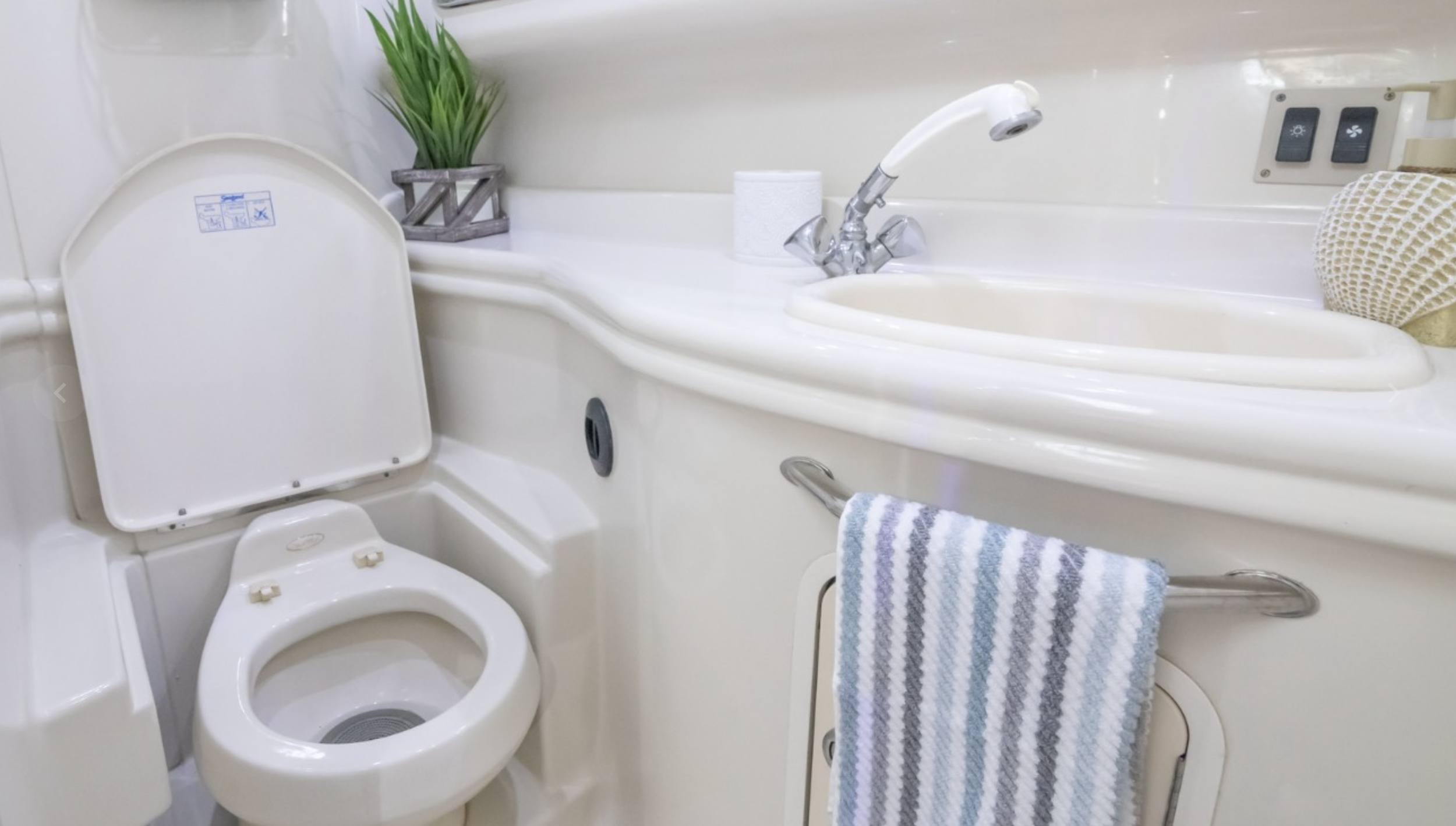 Small bathroom with a toilet, a small sink, a towel hanging on a rail, soap dispenser, decorative seashell, green plant, and electrical outlets.