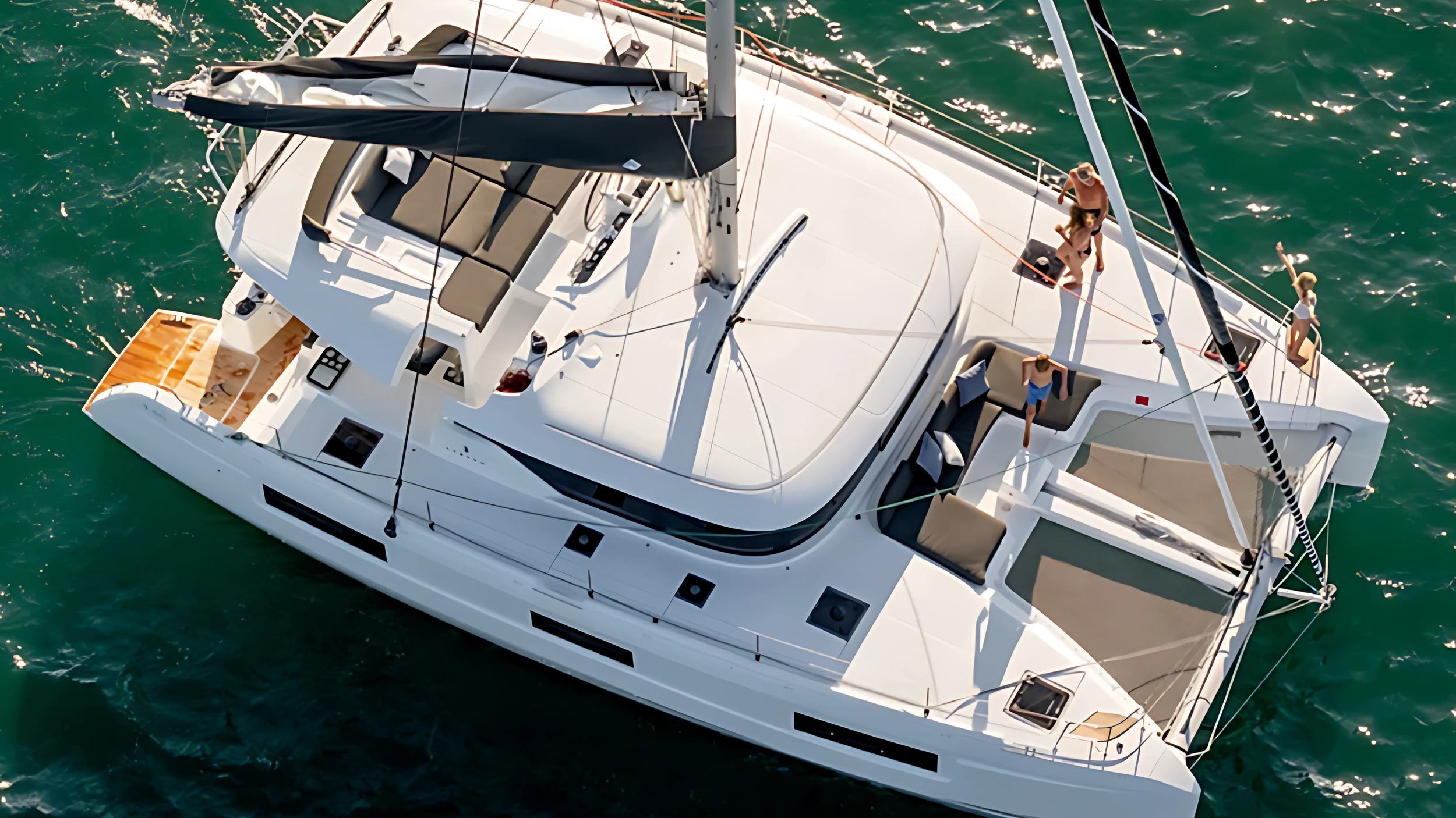 Aerial view of a white catamaran sailing with people relaxing on deck in the ocean.