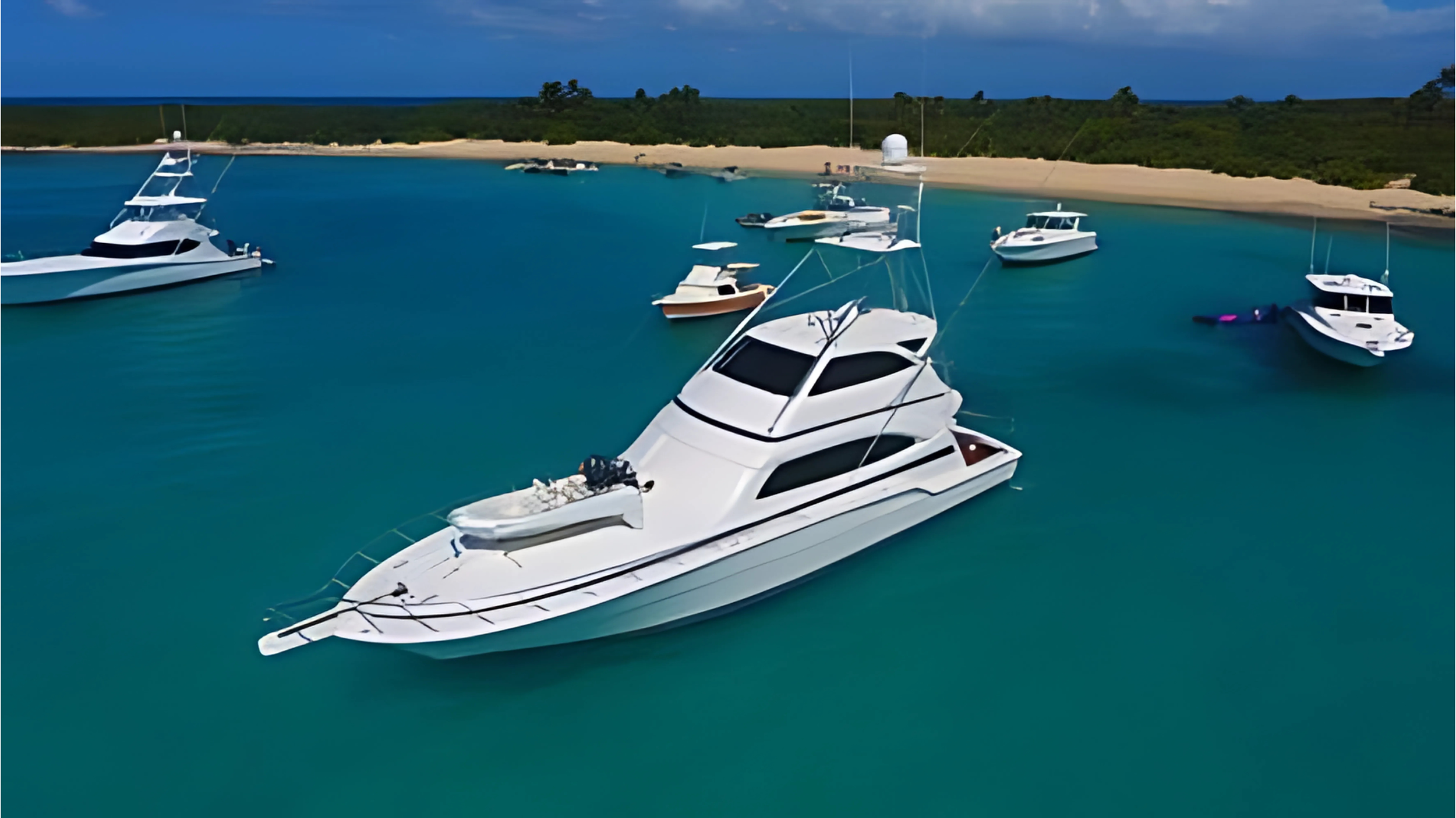 Several white yachts anchored in calm blue water near a sandy shoreline with green trees and a cloudy sky in the background.