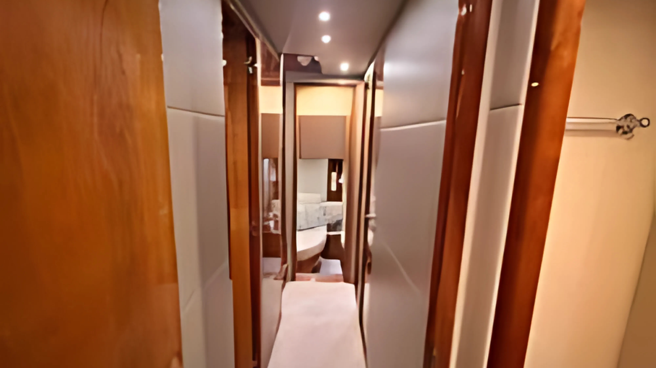 A narrow corridor inside a yacht or boat, with wooden paneling and doors leading to bedrooms and possibly a bathroom, shown in a mirror reflection.