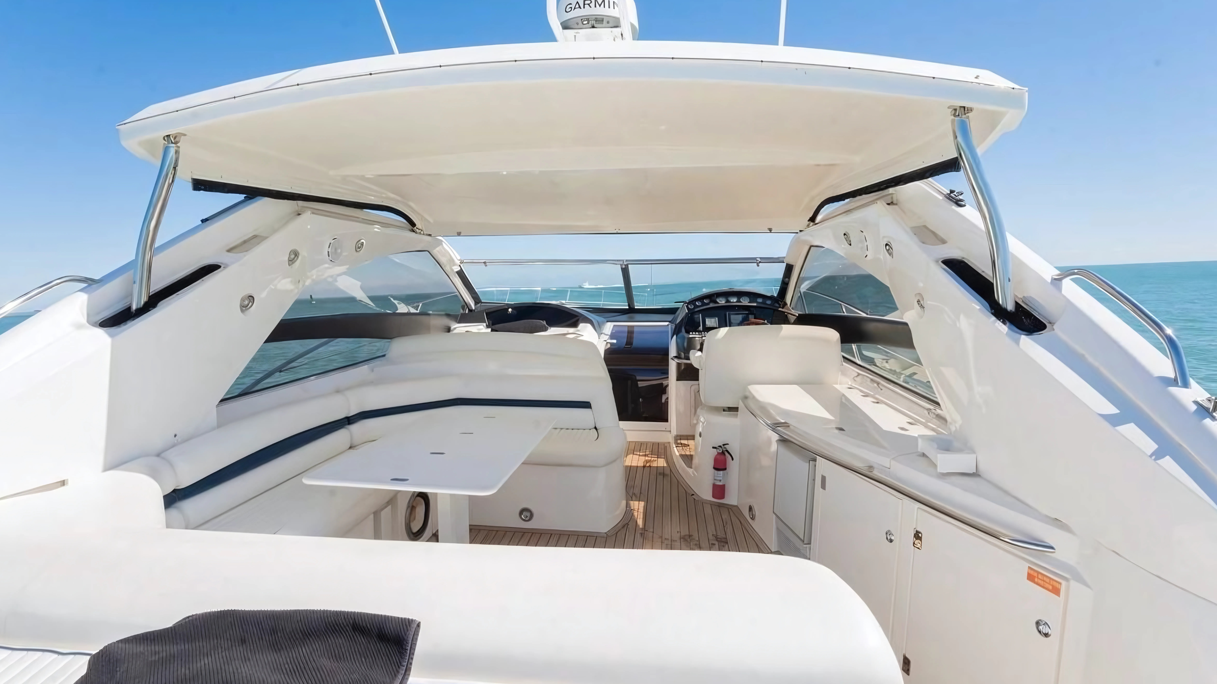 Interior of a luxury yacht with seating, table, and helm, set against a clear blue ocean sky.