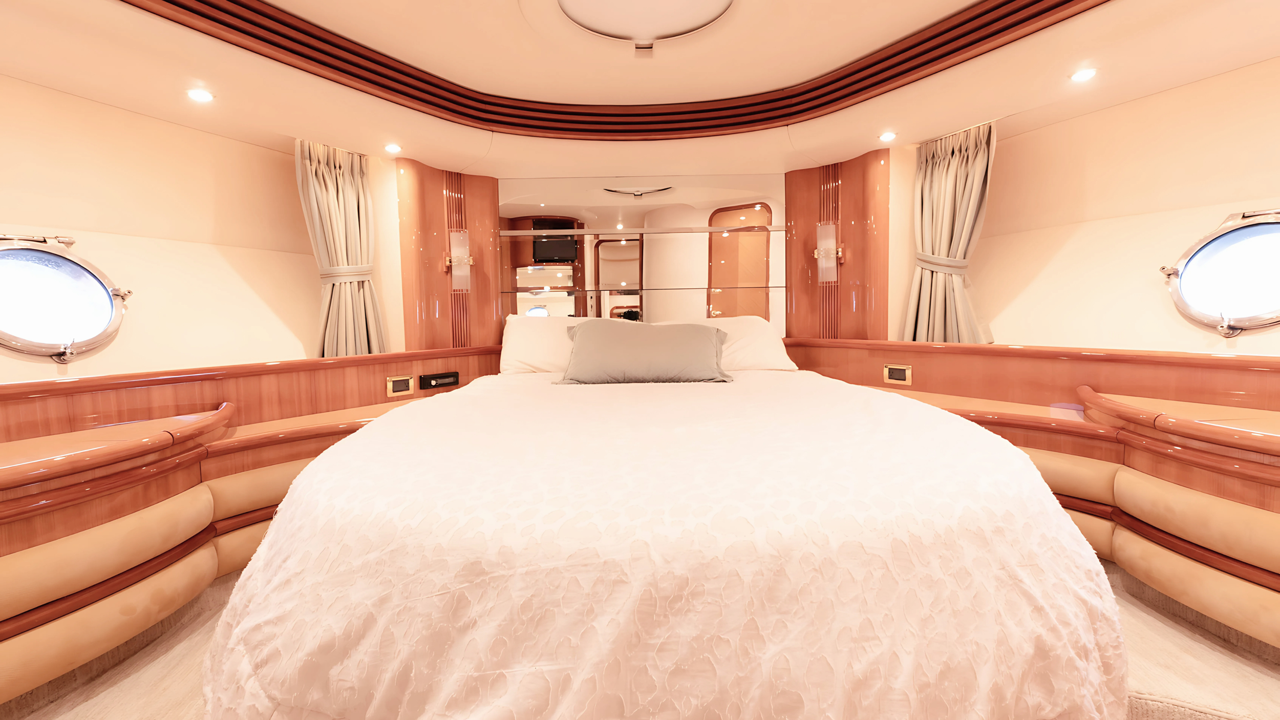Luxurious yacht cabin with double bed, wooden furnishings, and portholes