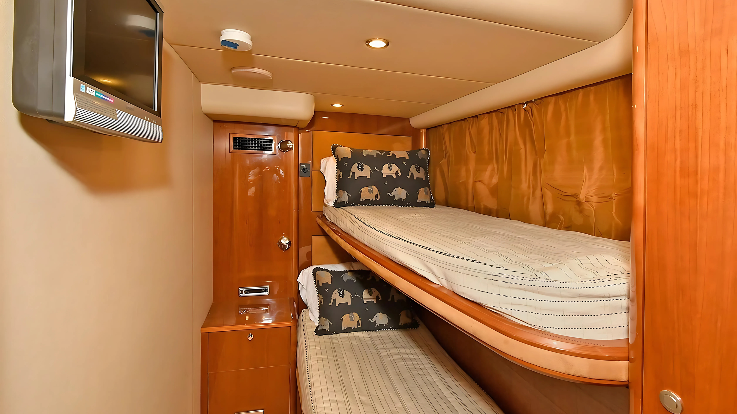 Compact cabin with bunk beds, elephant-themed pillows, a wall-mounted flat screen TV, and wooden furnishings.