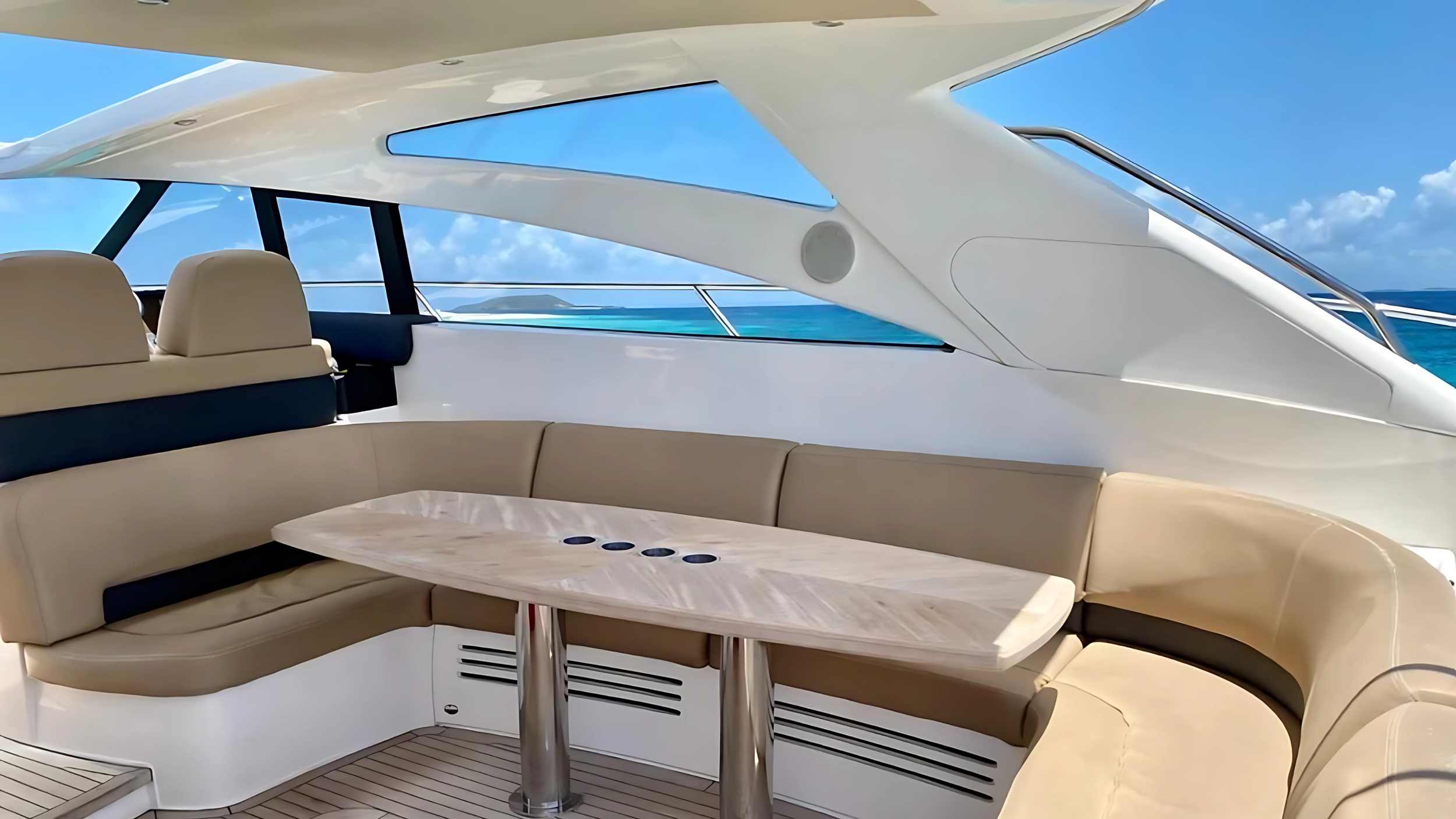 Interior of a luxury yacht with beige leather seating, a wooden table, large windows, and ocean view.