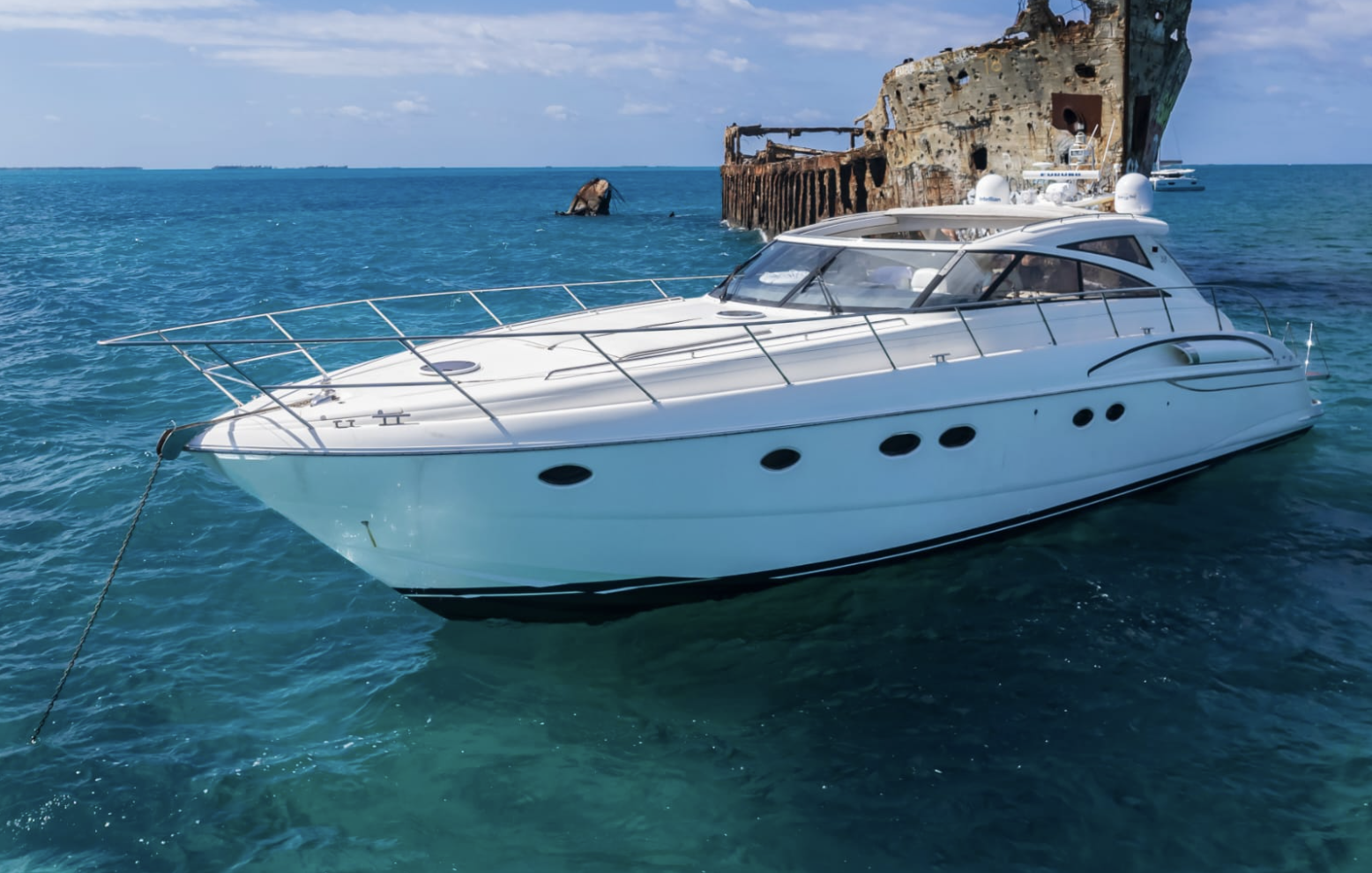 A white yacht floating on clear blue water near an old shipwreck.