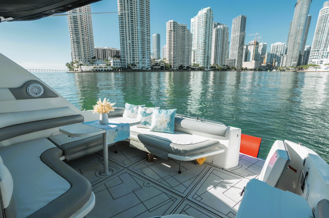Luxury yacht deck with seating and table, view of city skyscrapers across water.