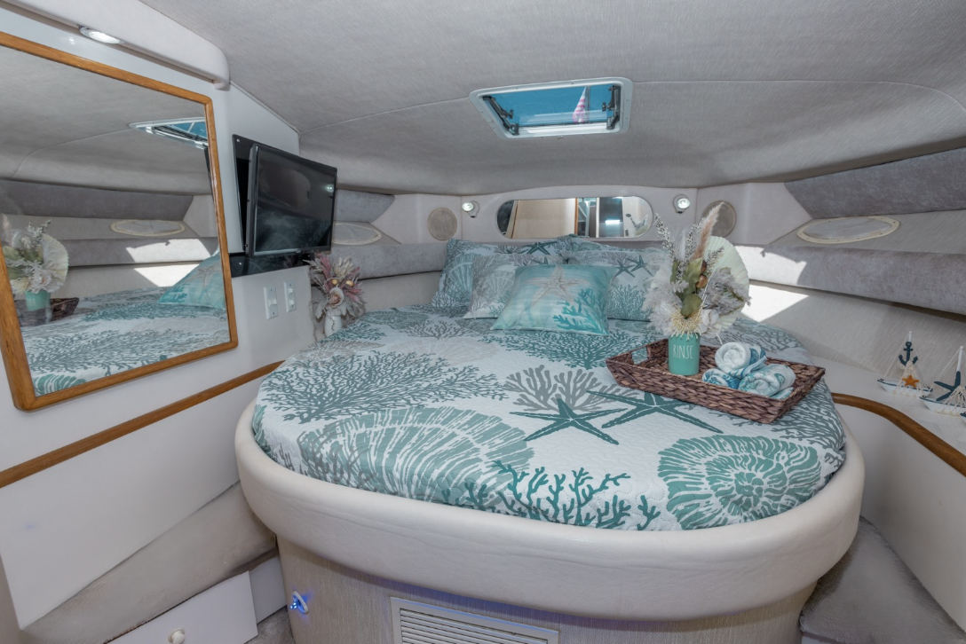 Interior of a boat cabin with a circular bed, marine-themed bedding, wall-mounted TV, mirror, and decorative items.