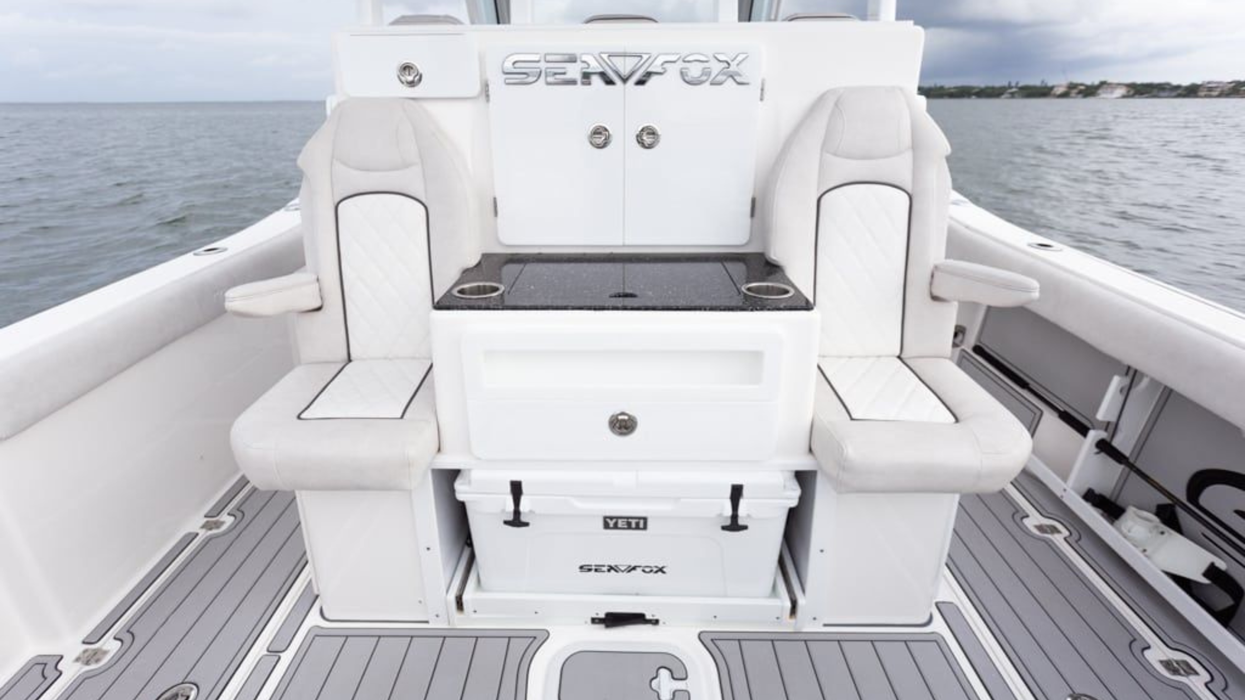 Interior of a boat showing two cushioned seats, a center console with a storage area, and a Yeti cooler under the bench, with a calm sea in the background.
