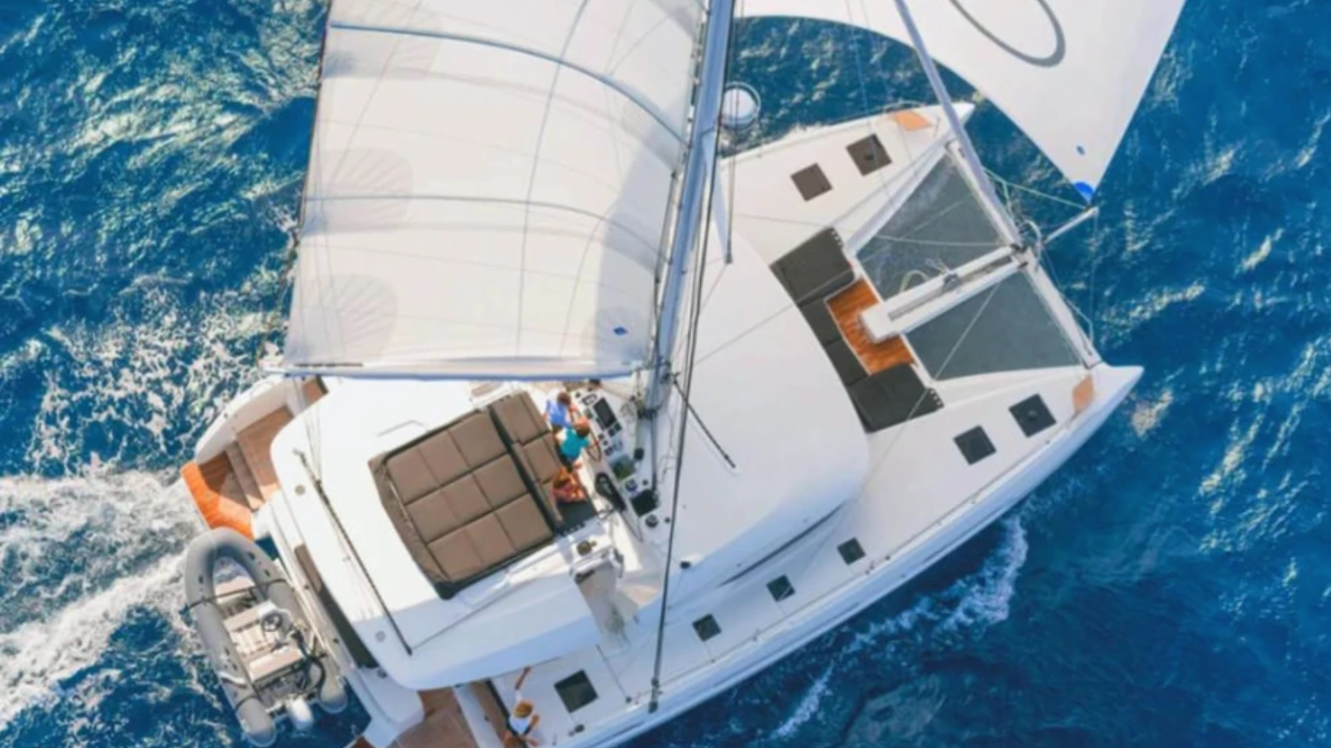 Aerial view of a sailing catamaran on the ocean with white sails, people on deck.