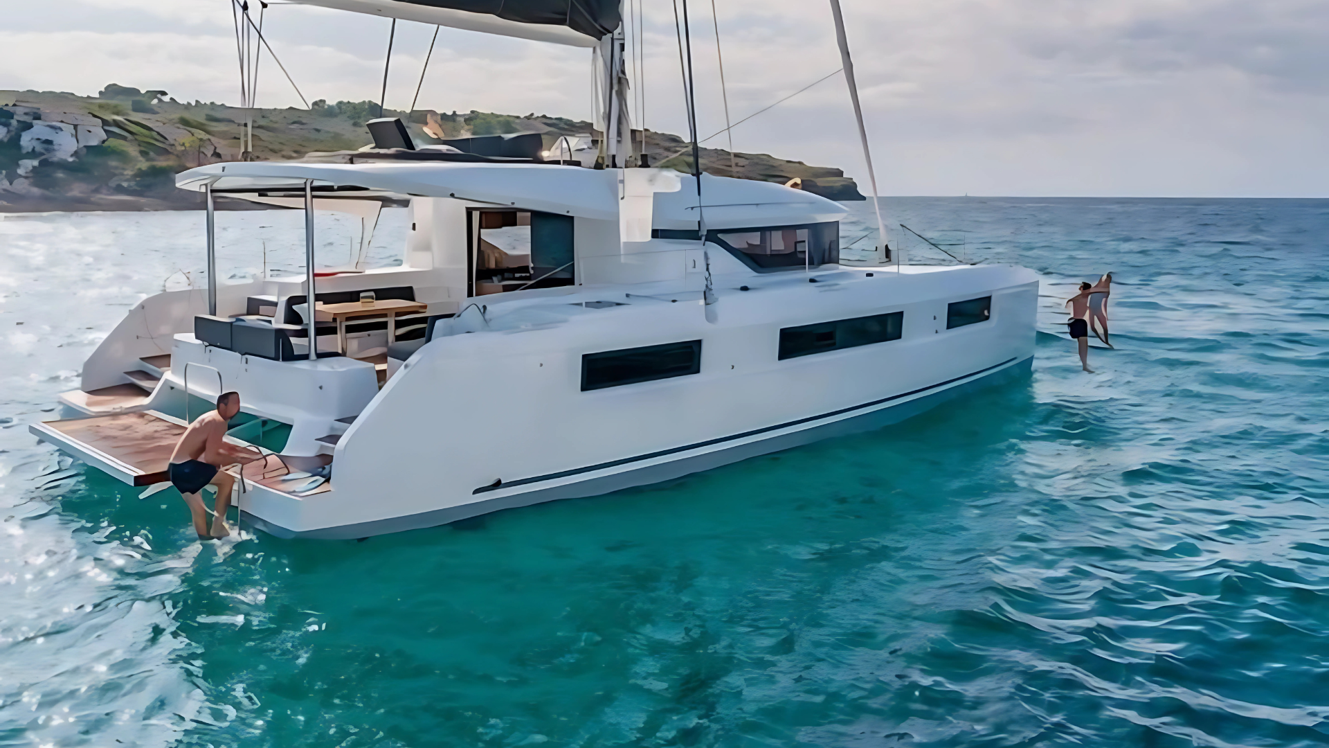 Catamaran on clear blue water with people swimming and lounging.