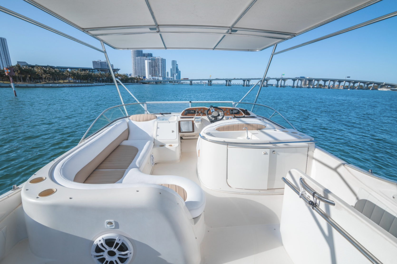 Luxury yacht interior with seating and control panel on water with cityscape view.