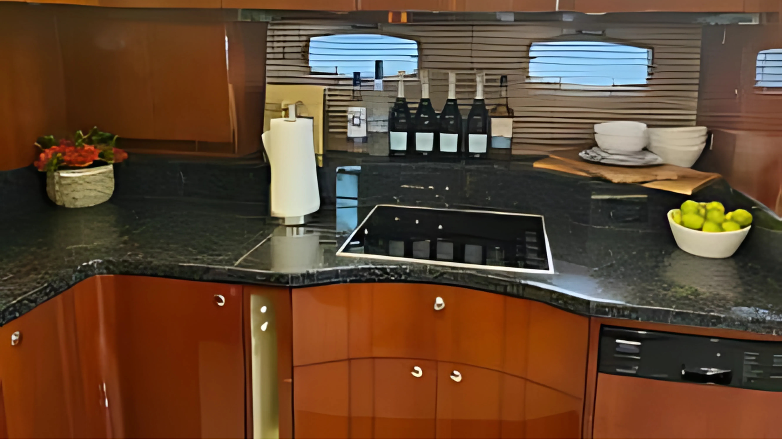 Kitchen countertop with bowls, bottles, paper towel, and fruit, with a window in the background.