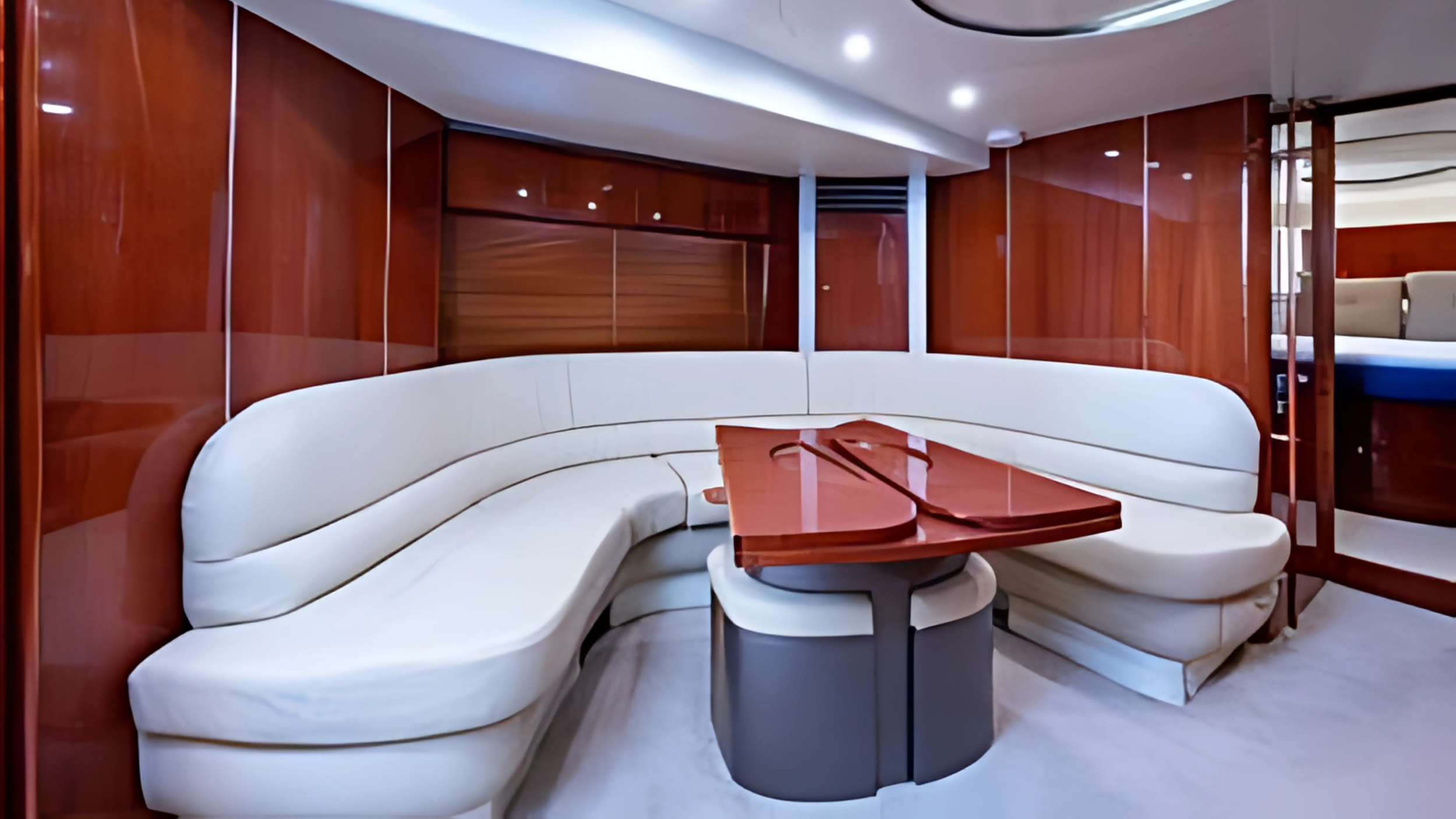 Interior of a yacht with a curved white leather sofa surrounding a wooden table.