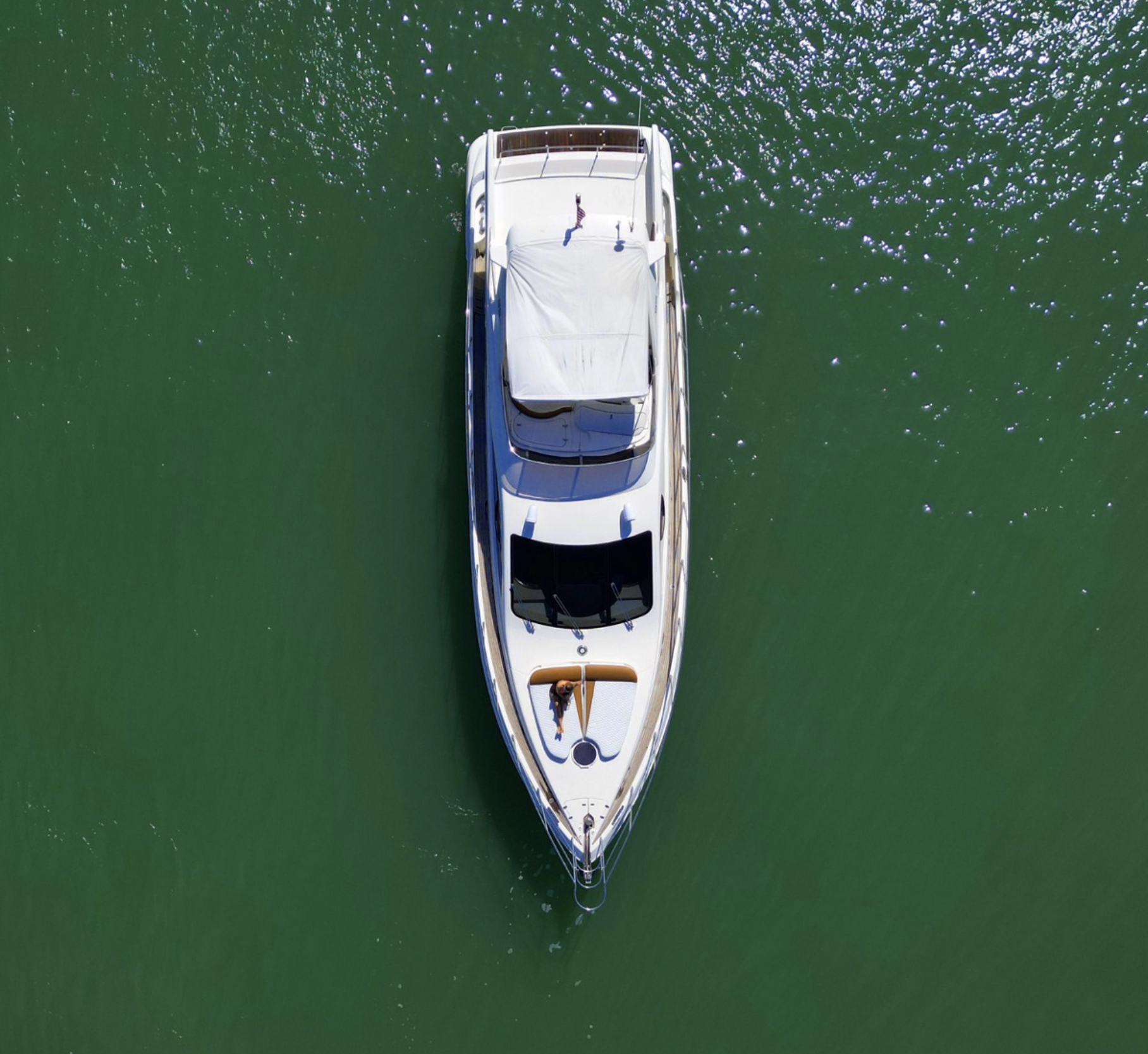 An aerial view of a white yacht floating on green water with a person on deck.