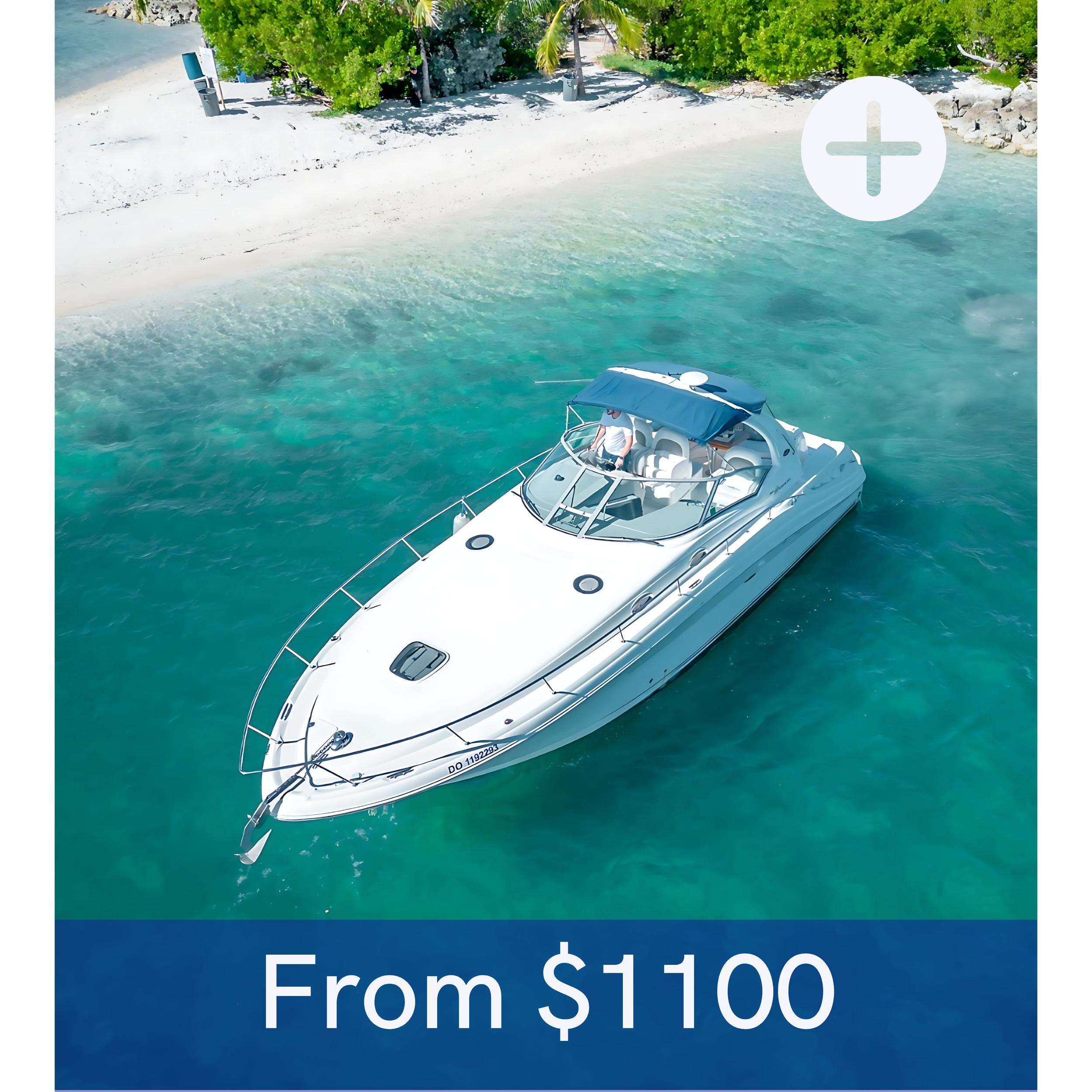 A white yacht floating in clear turquoise water near a sandy beach with lush green trees.