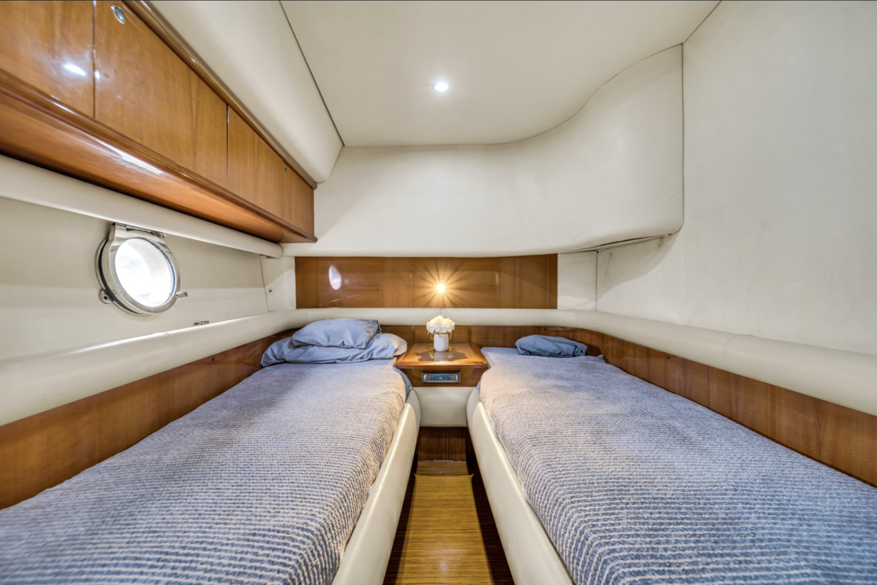 Yacht cabin interior with two twin beds, wooden paneling, and a small round window.