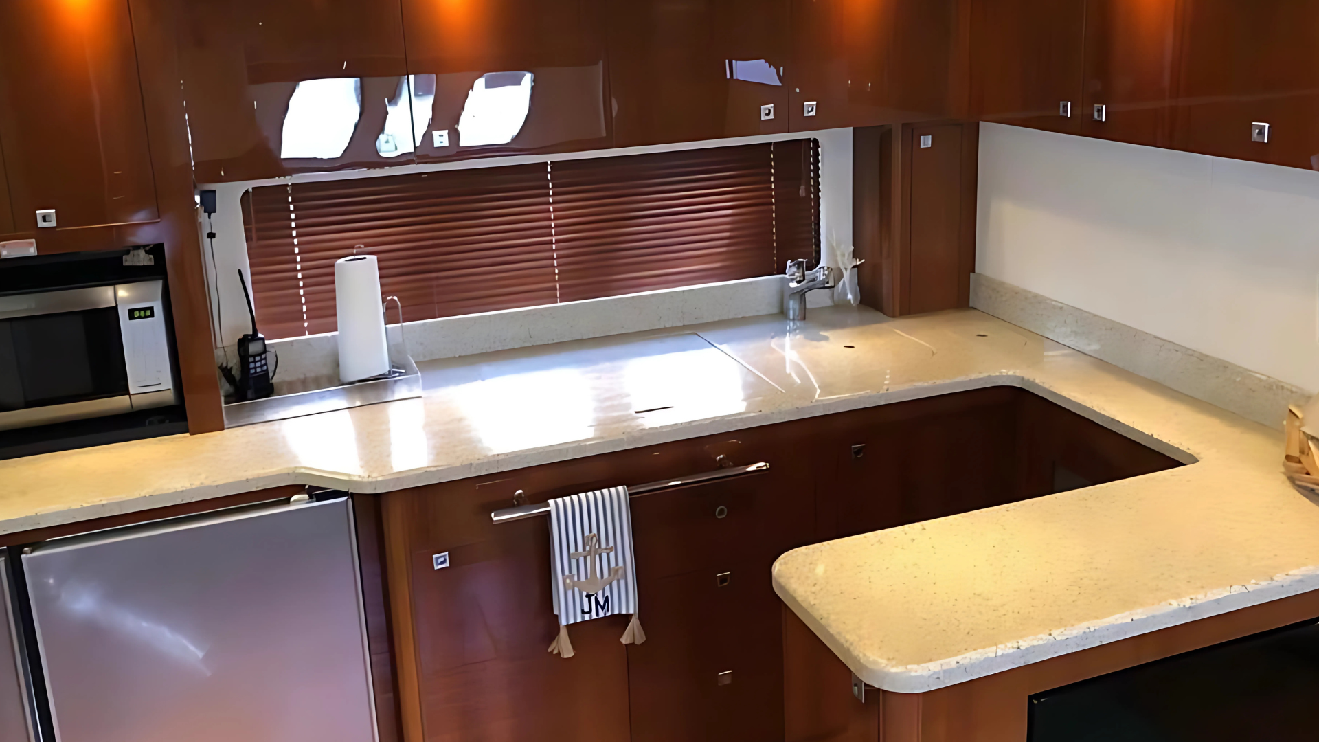 Modern kitchen interior with wooden cabinetry, marble countertops, built-in appliances, and a paper towel holder.