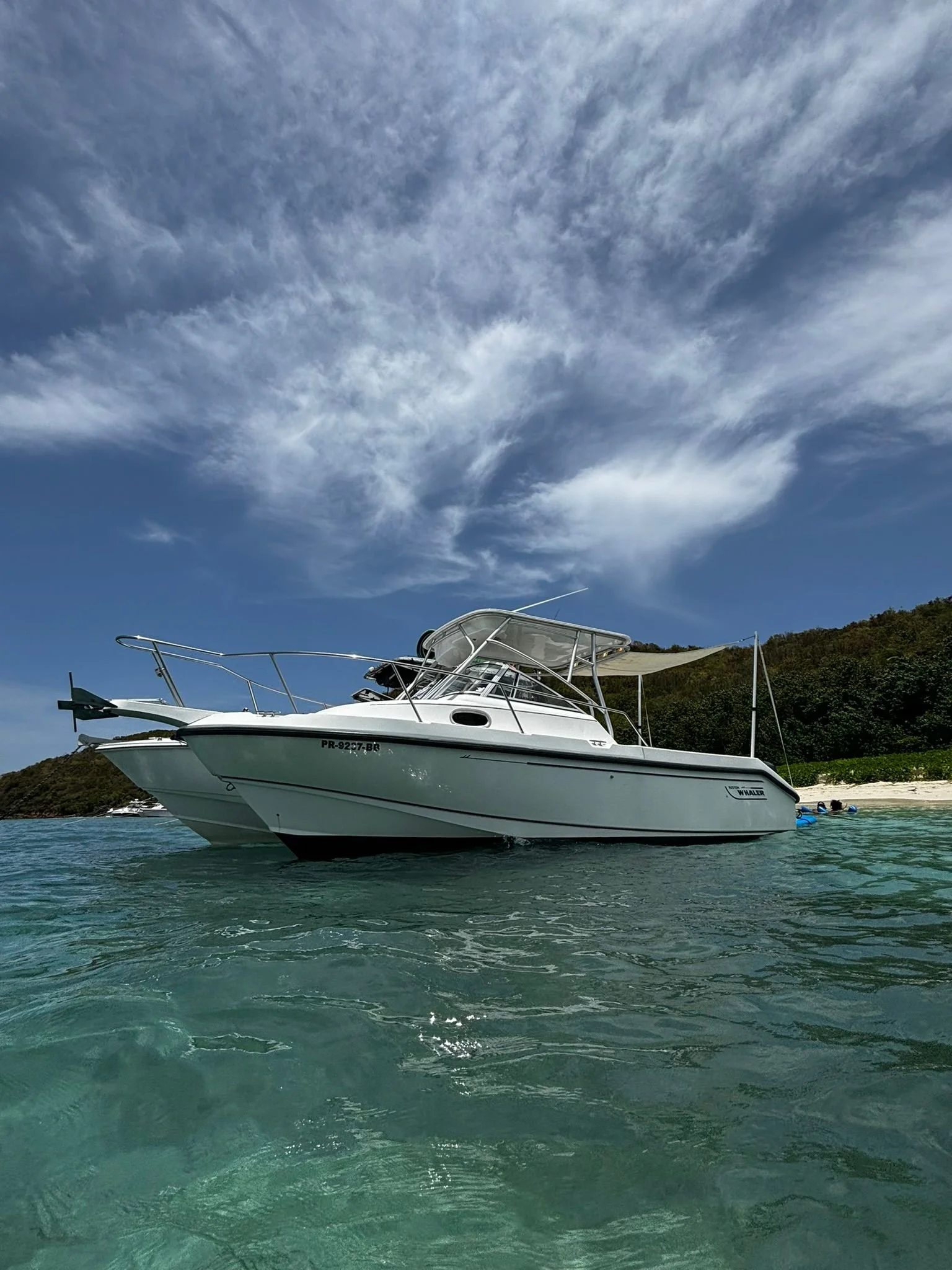 White motorboat on clear blue water near a beach with cloudy sky.