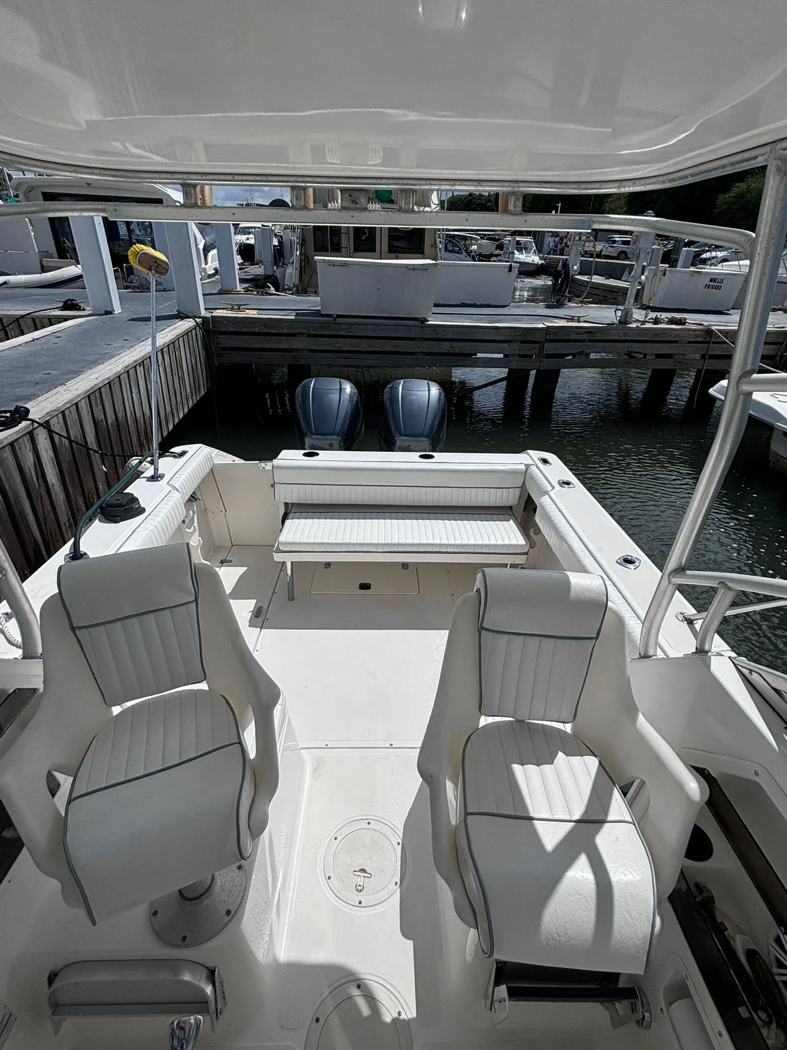 Interior of a small motorboat with two white cushioned chairs and two visible outboard motors near a marina dock.