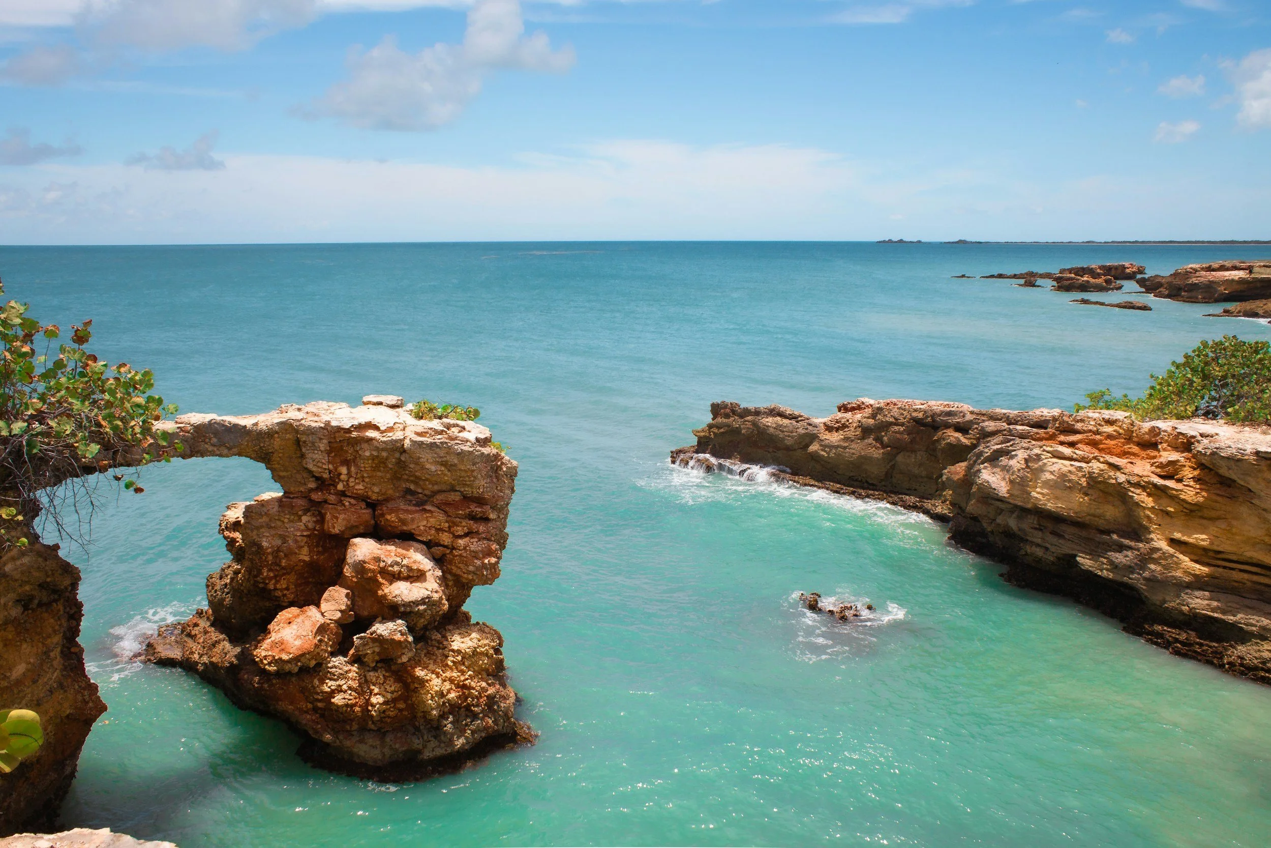 Tropical coastline with turquoise water, rocky cliffs, and a clear sky with some clouds.