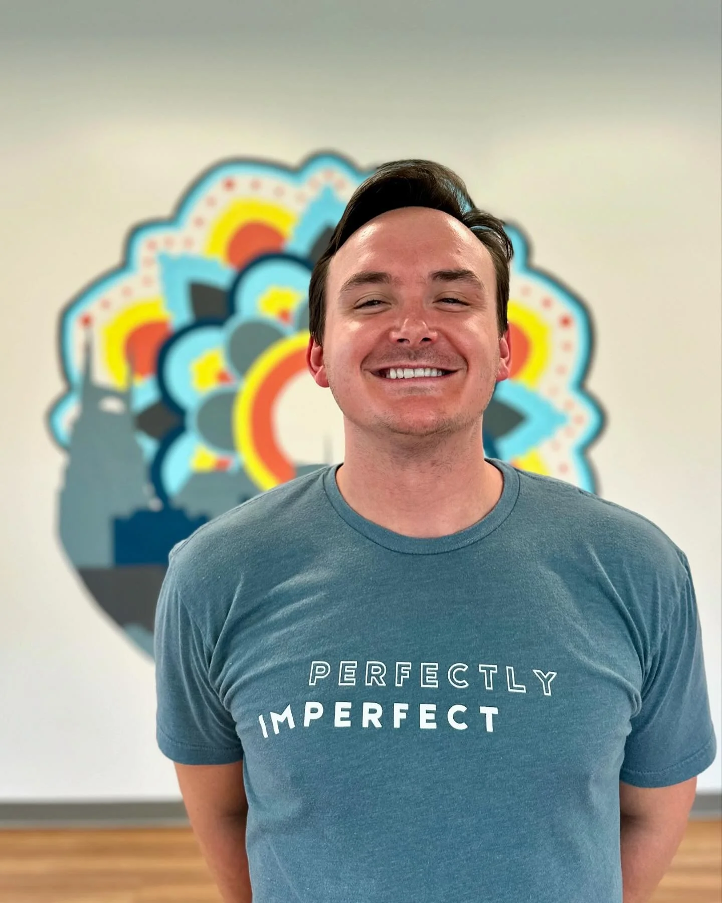 A smiling young man with short dark hair standing in front of a colorful, abstract wall art