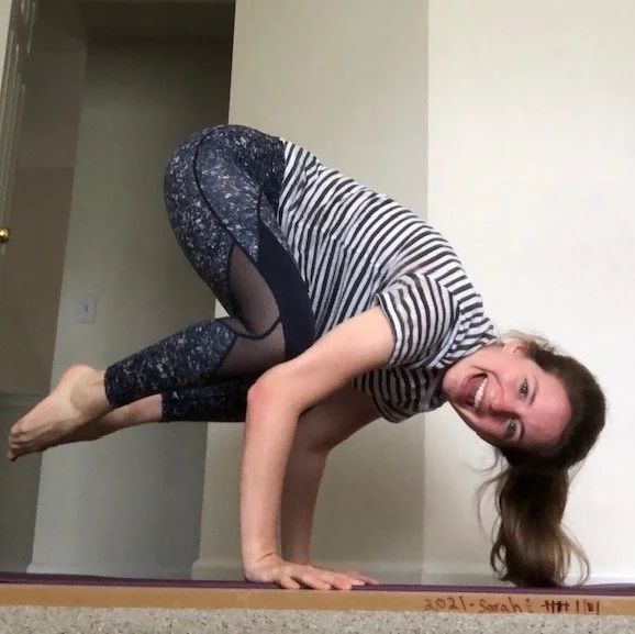 Woman in striped shirt and patterned leggings performing a yoga pose in a room.