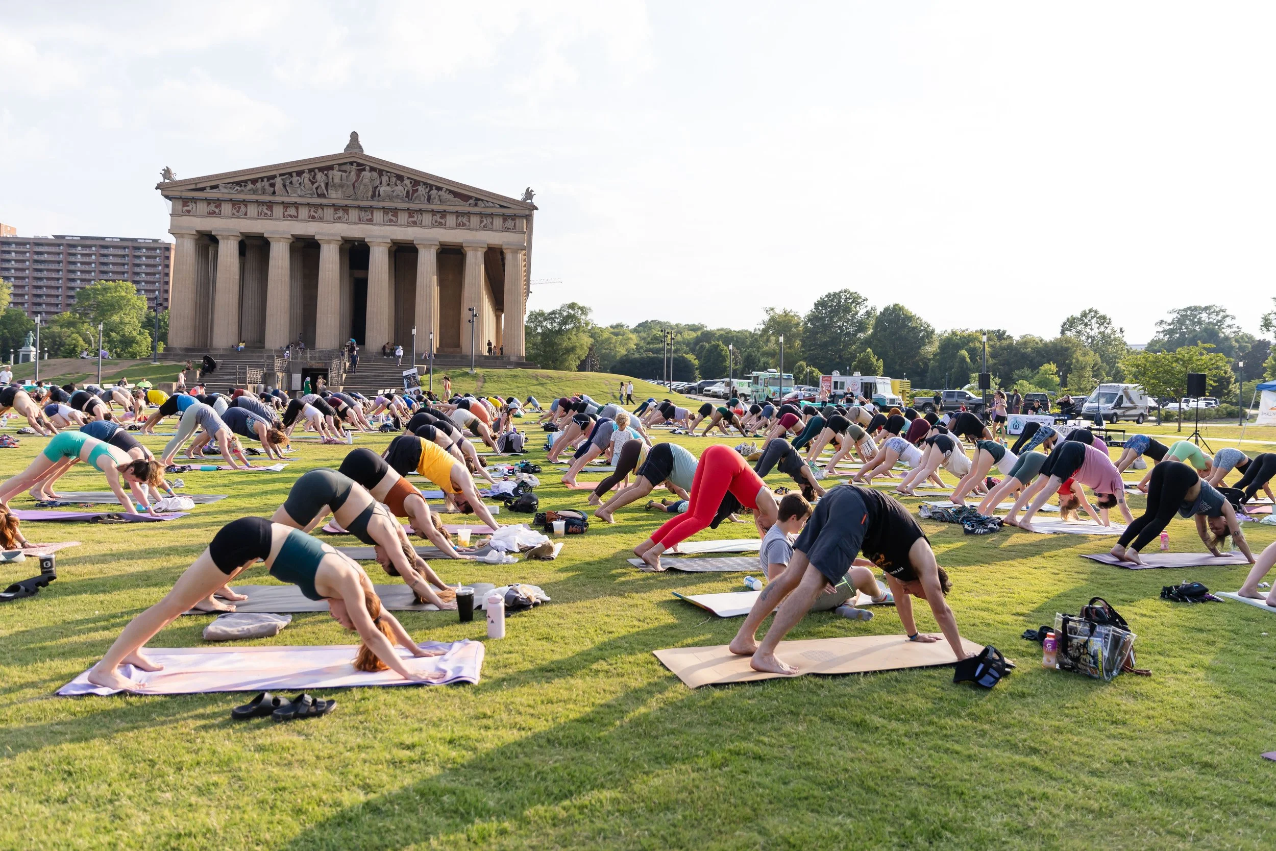 People participating in an outdoor yoga class on the lawn in front of the Parthenon replica at Centennial Park, Nashville, Tennessee, during daytime.