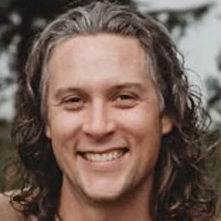 A man with long, curly hair smiling outdoors.