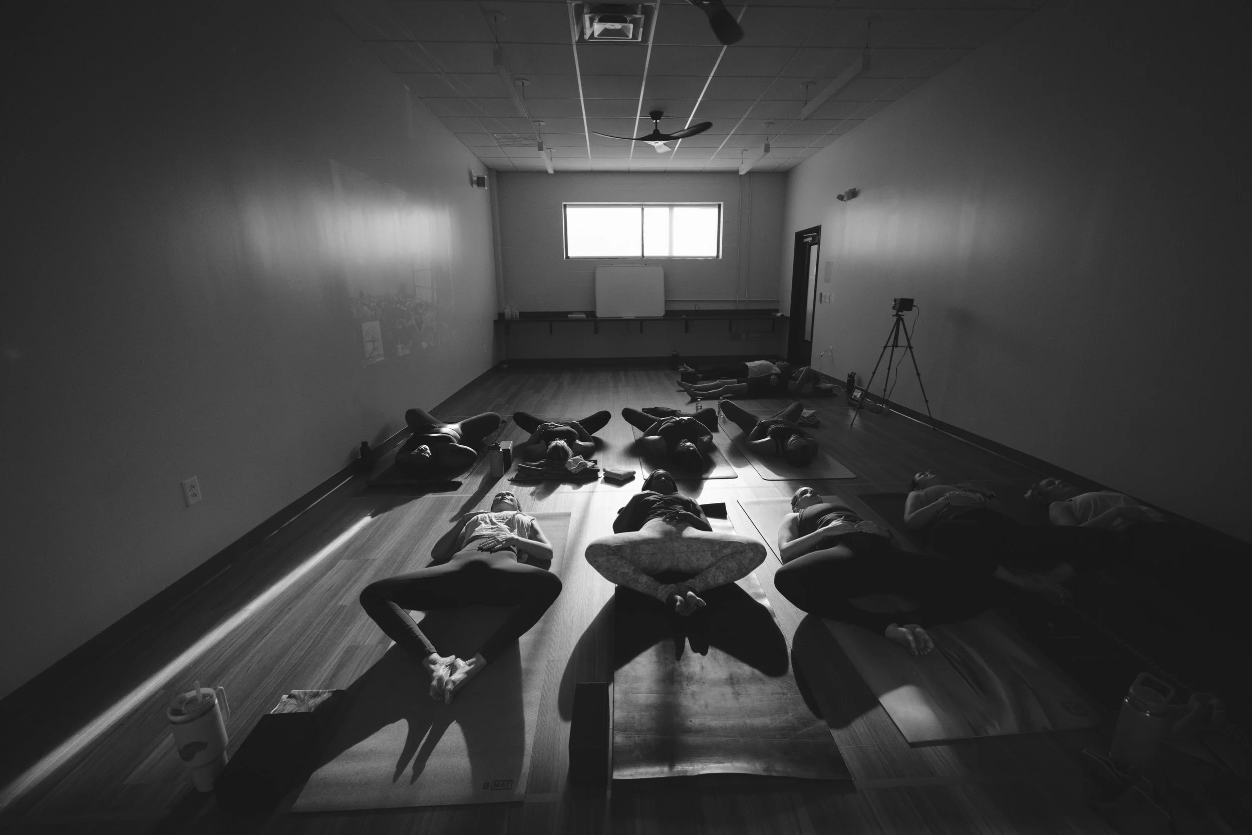 People participating in a yoga or meditation class lying on yoga mats in a dimly lit room.