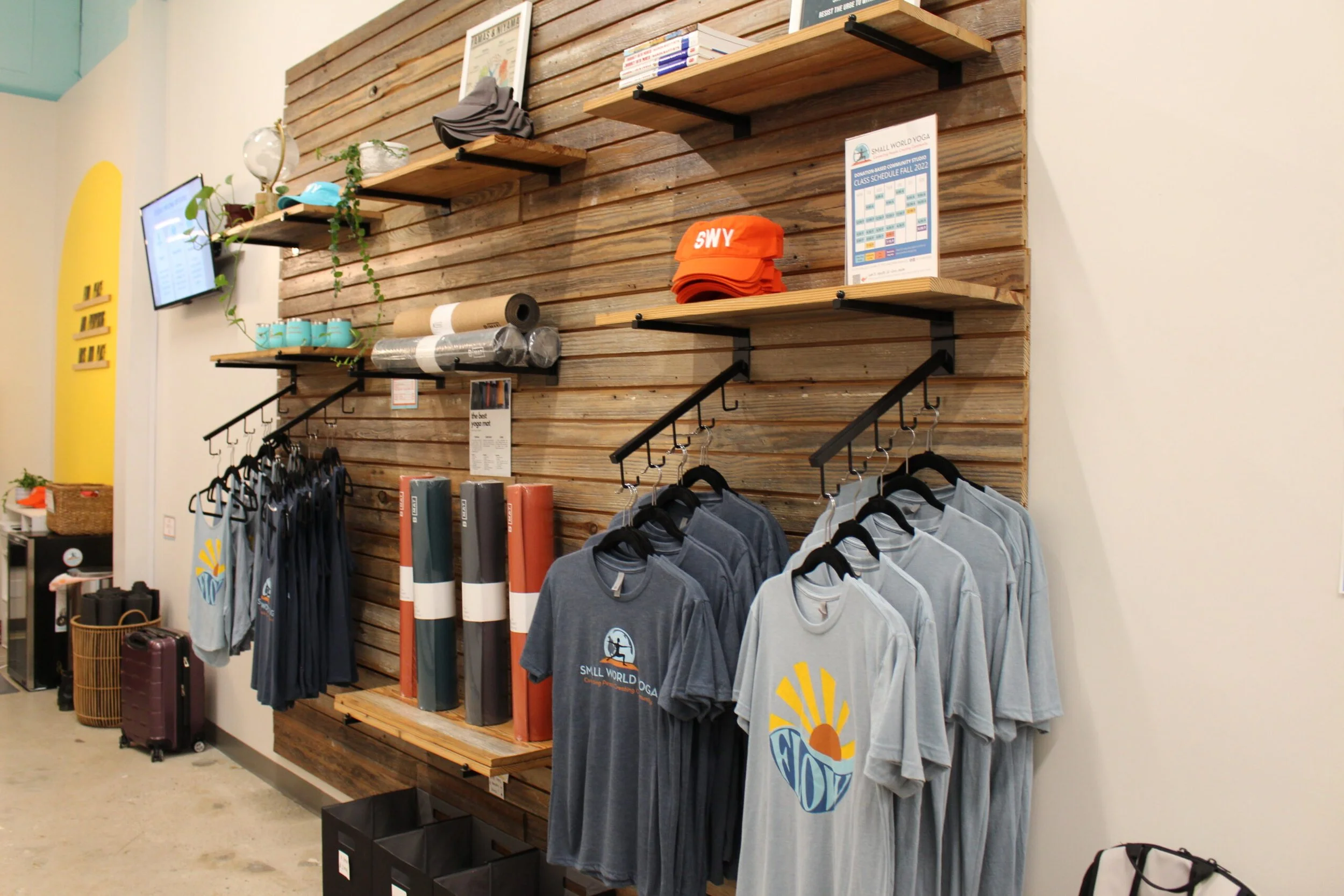 Display of clothing and accessories on a wooden wall, including t-shirts, hats, and yoga mats at a retail store.