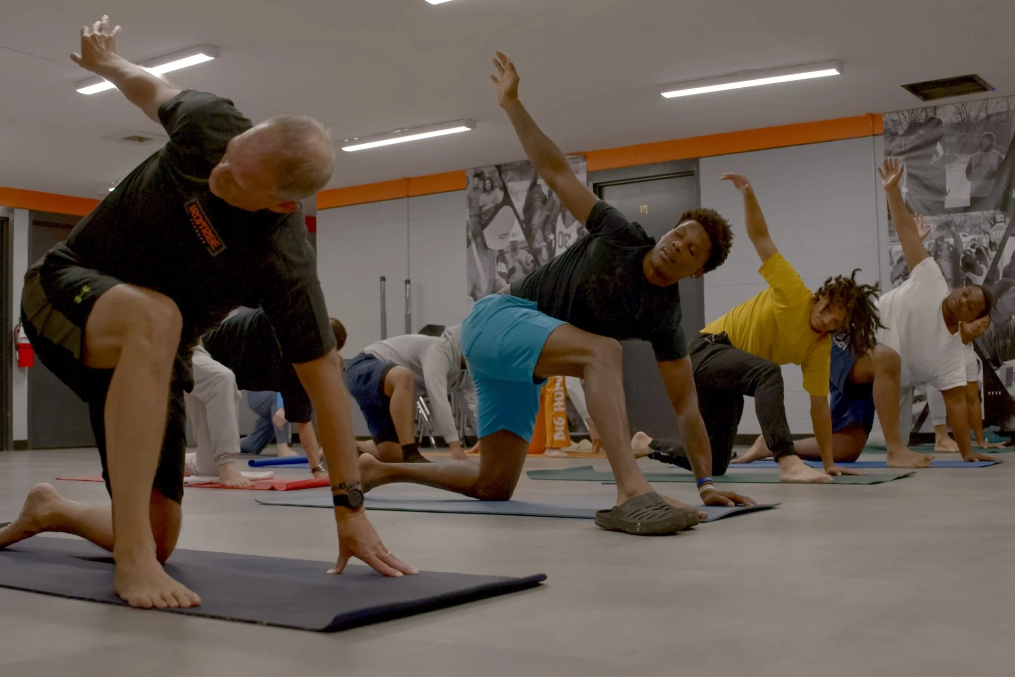 Group of people participating in a yoga class, doing a modified downward dog pose on mats in a studio with black and white photographs on the walls.