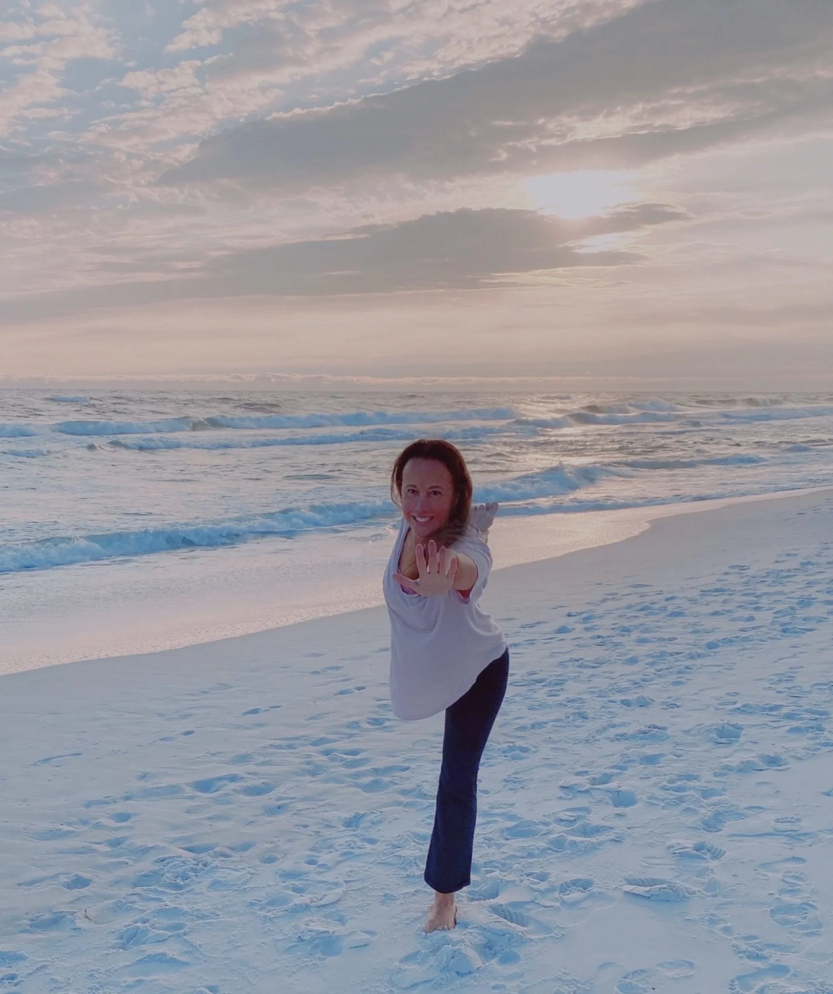 Woman practicing yoga on a sandy beach during sunset