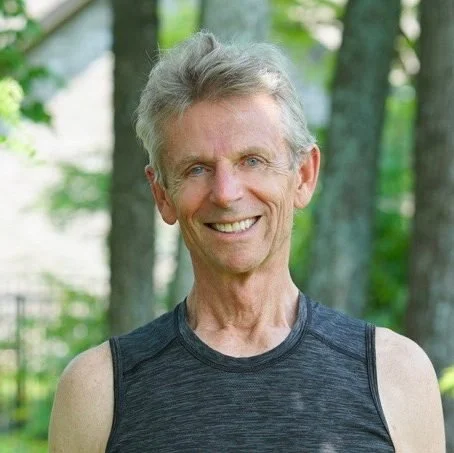 Smiling elderly man in sleeveless athletic shirt outdoors with trees in the background.